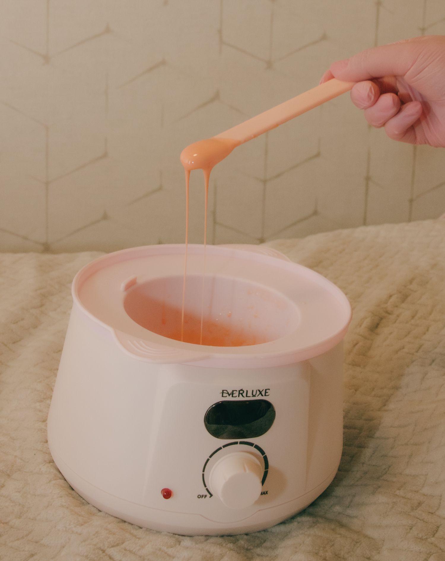 White wax warmer pot with melted pink wax being tested with applicator stick.