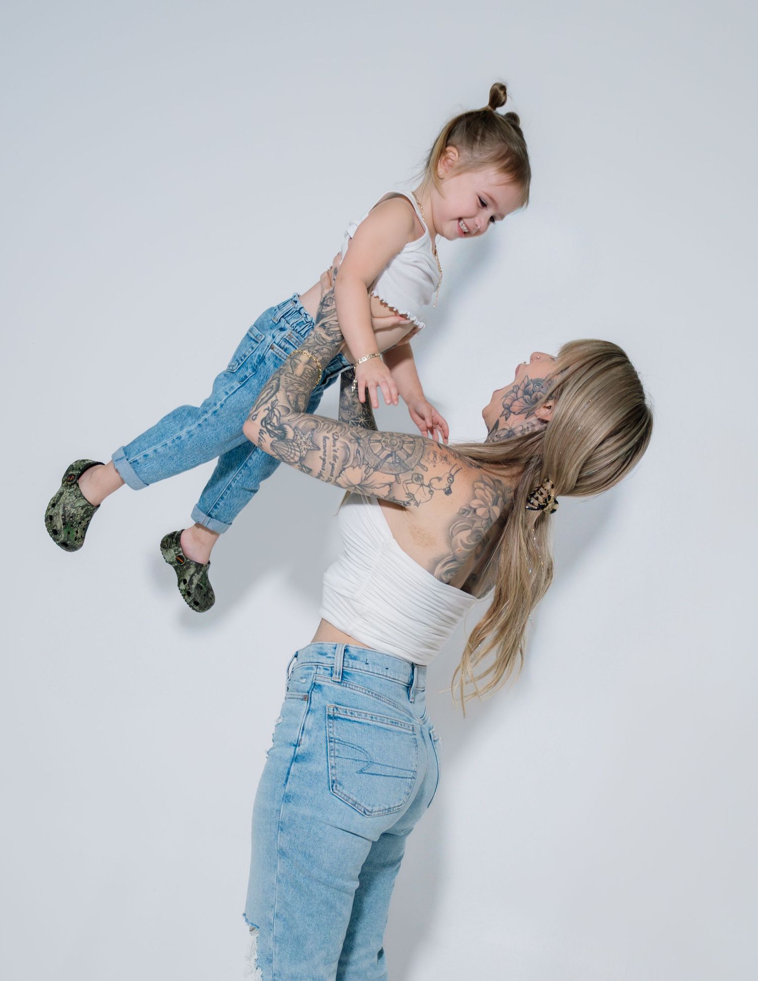 A playful sequence showing a child jumping and leaning on an adult in light-colored clothing against a white backdrop.