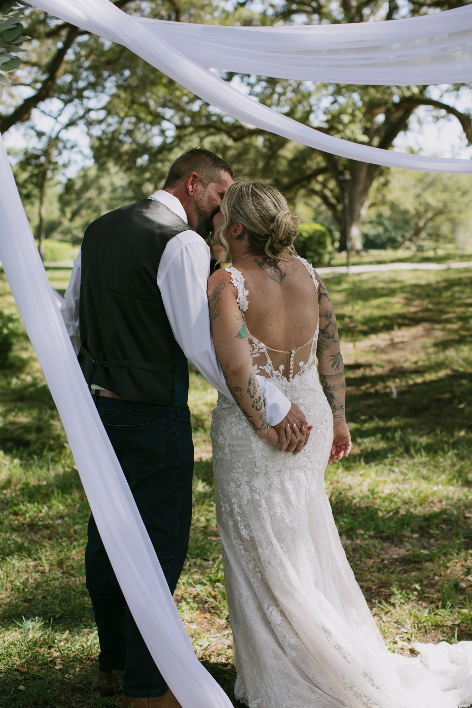 A romantic outdoor wedding scene under a flowing white fabric arch with a couple embracing in nature.