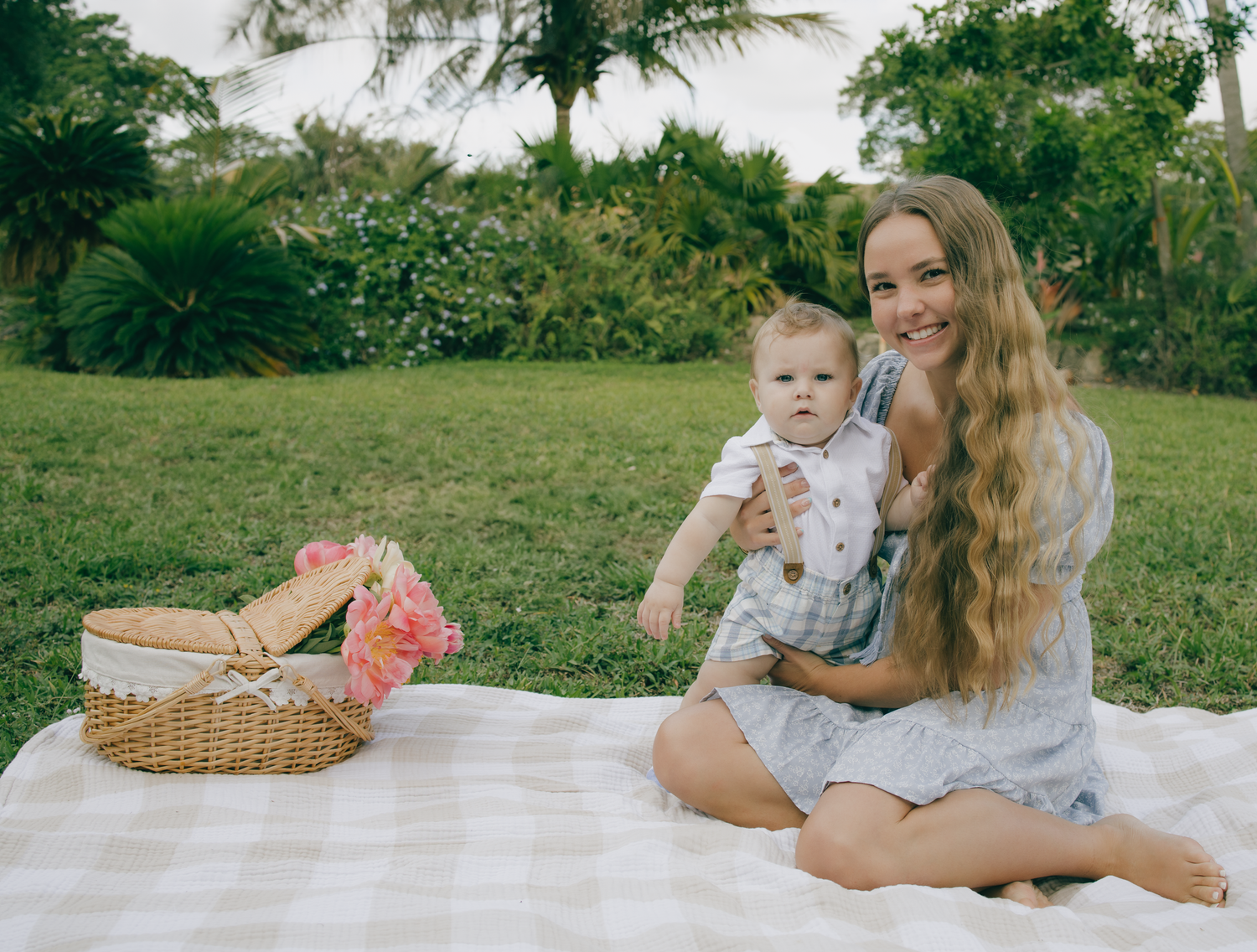 A picnic scene with mother and baby on a checkered blanket with a basket of flowers.