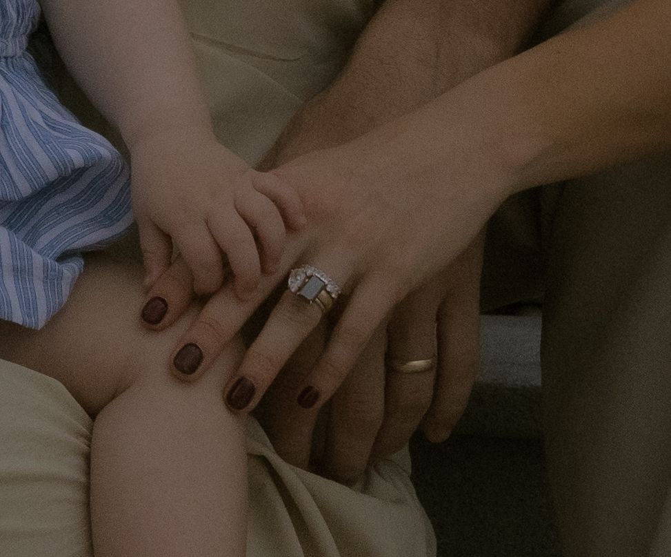 Close-up view of hands with dark nail polish resting on soft fabric in dim lighting.