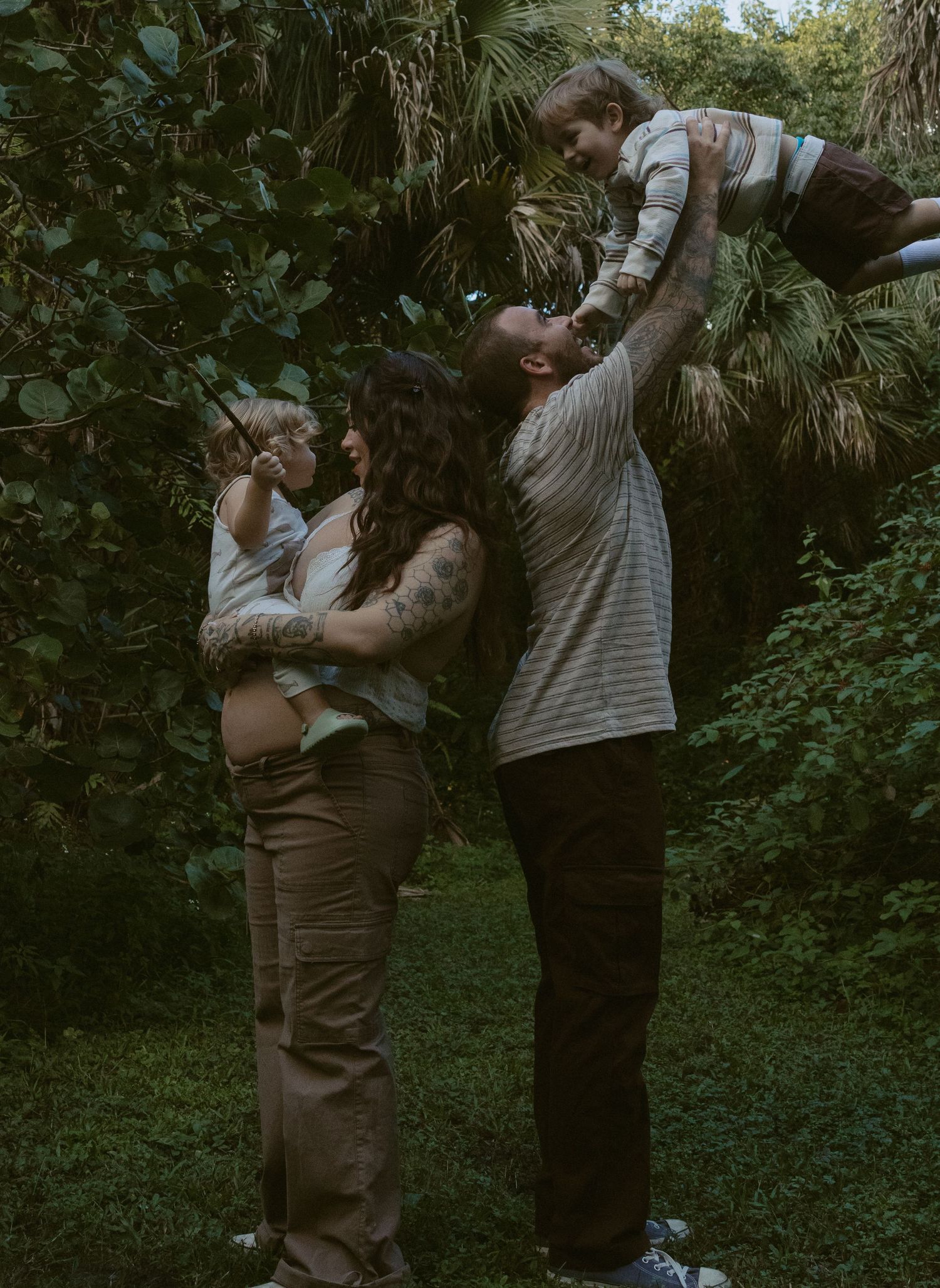 A couple shares a tender moment in a lush green forest setting during what appears to be an engagement photoshoot.
