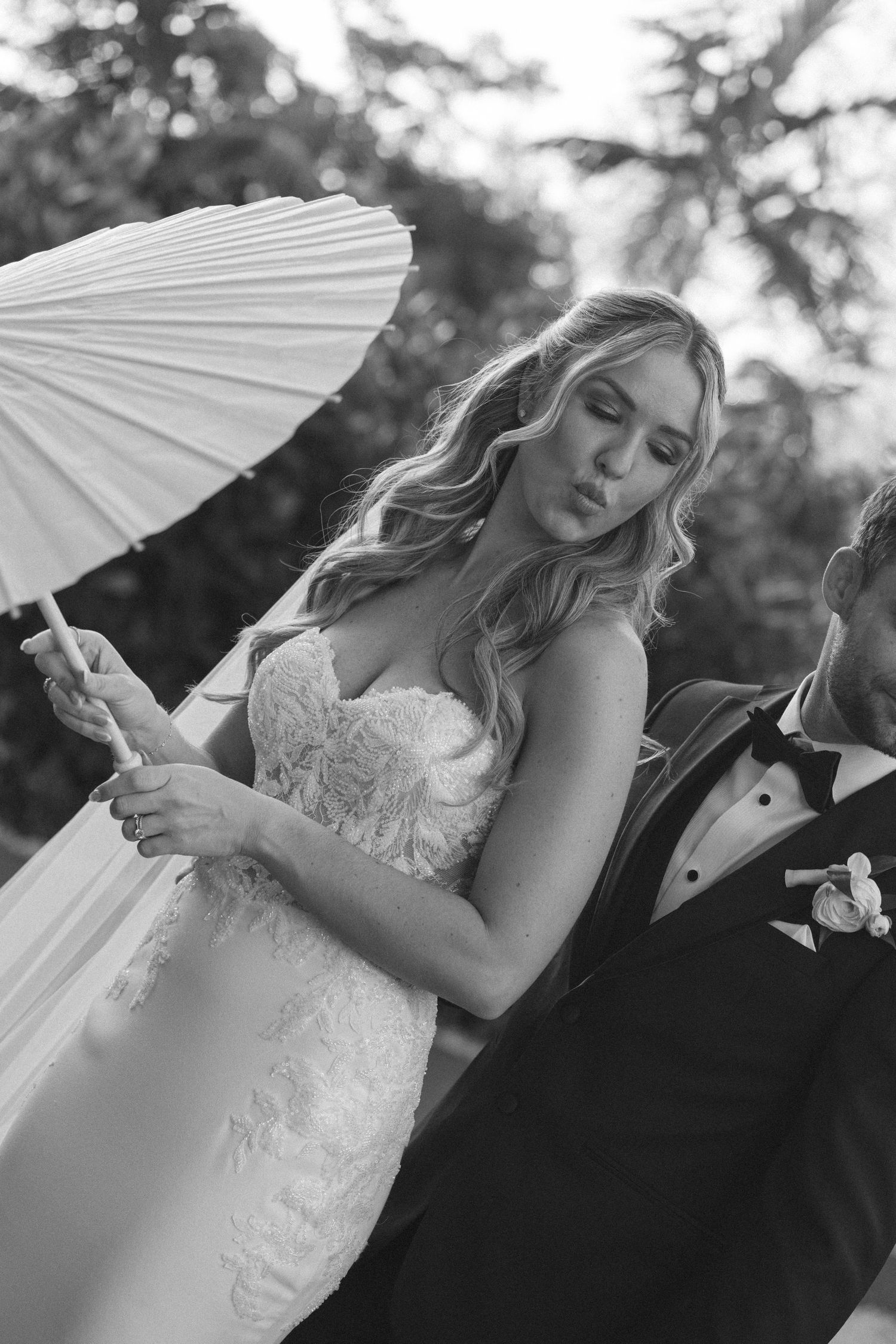 A romantic black and white wedding photo series showing a couple with a white parasol sharing intimate moments outdoors.