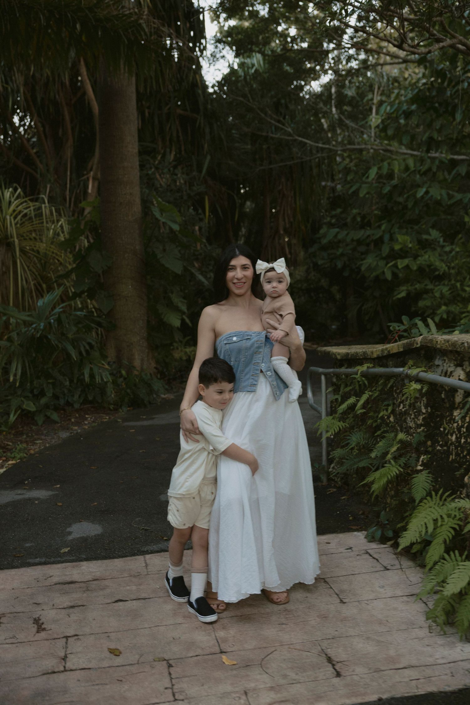 Two people in white dresses share a tender moment together on a stone patio surrounded by lush greenery.