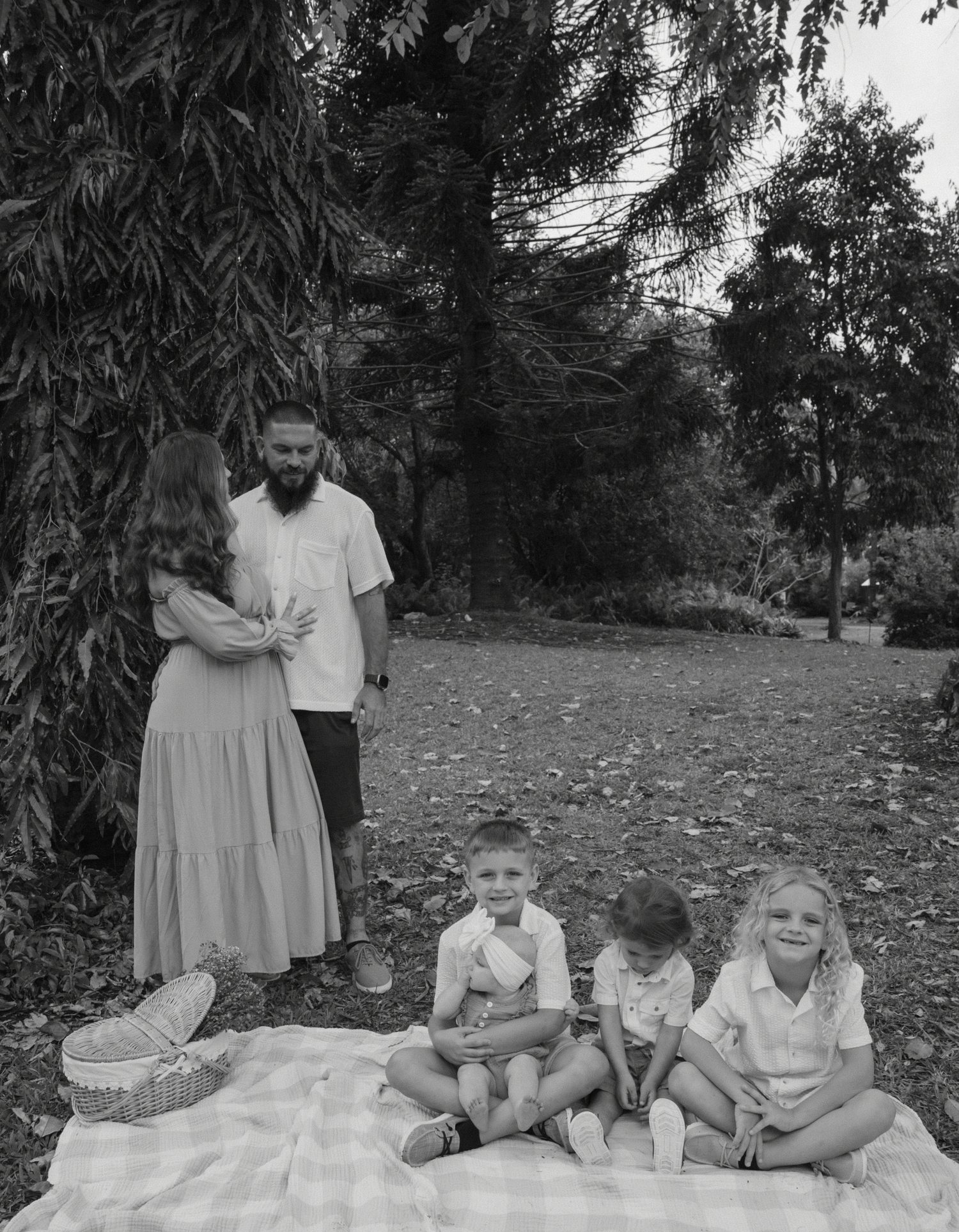 A black and white photo series showing a family sitting together on a blanket outdoors in a natural setting.