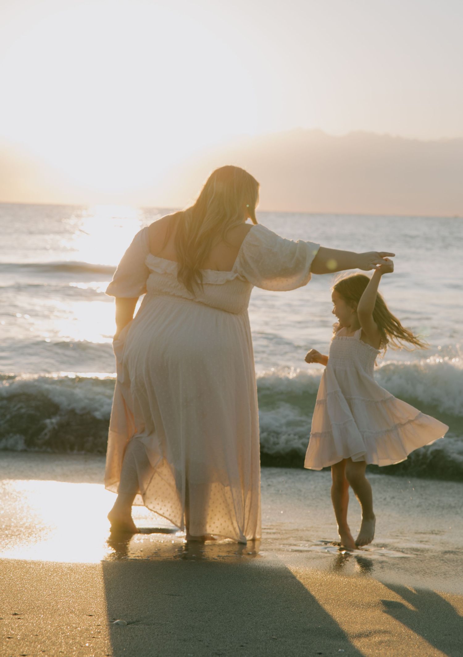 Silhouettes of people in white attire playing on a beach at sunset with golden light reflecting off the ocean waves.