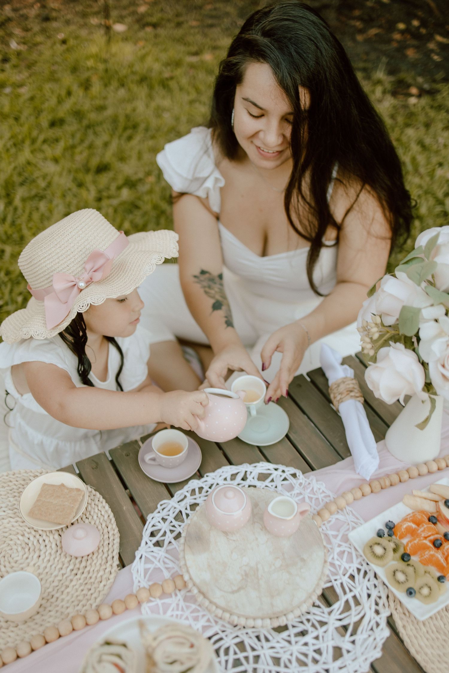Mother and daughter enjoying a whimsical garden tea party with pink and white decorations.