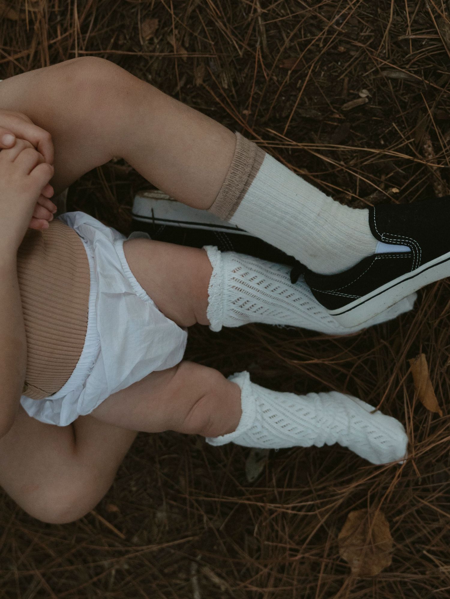 Person wearing white knee-high socks and a light-colored dress lying on dried grass and leaves.