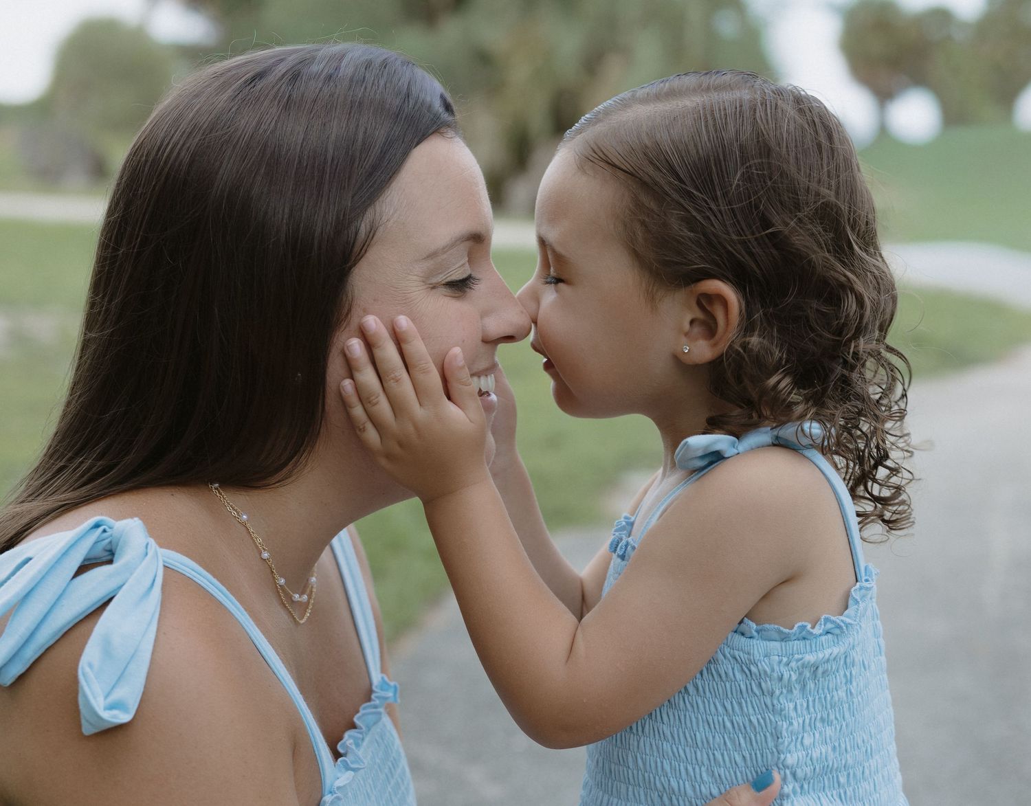 A tender moment captured in a series of five photos showing two people in light blue outfits sharing a sweet kiss outdoors.