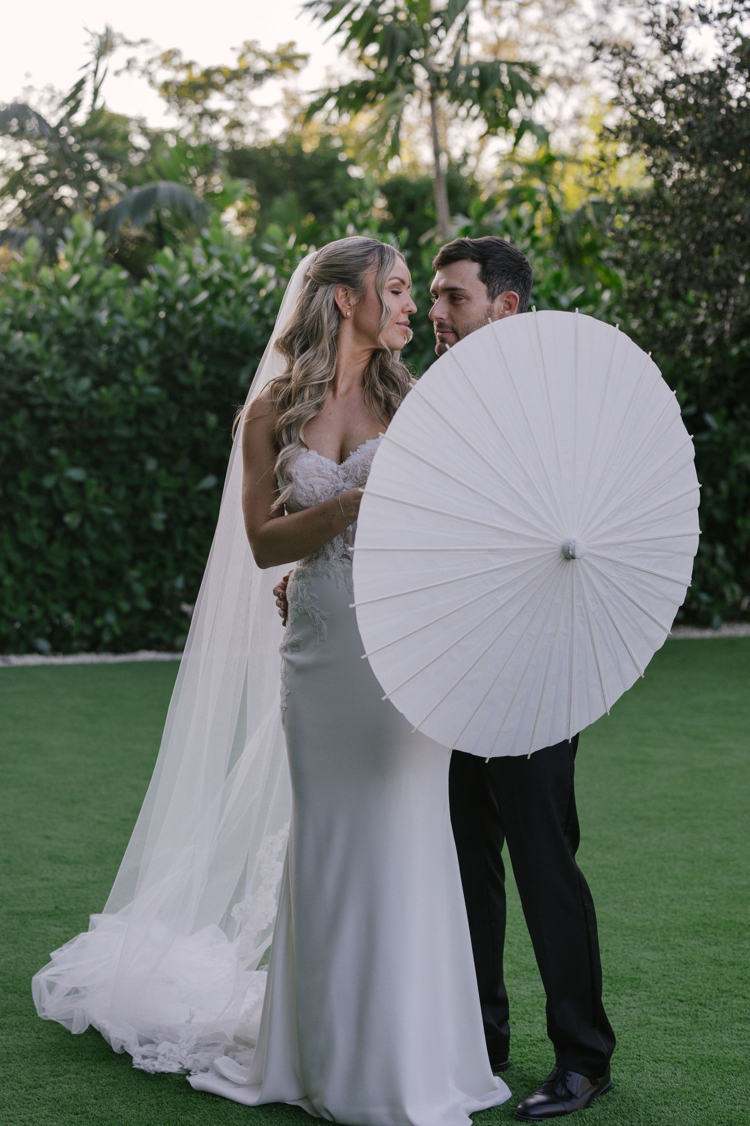 A romantic wedding scene on a lawn with a flowing white gown and elegant white parasol creating dreamy moments.