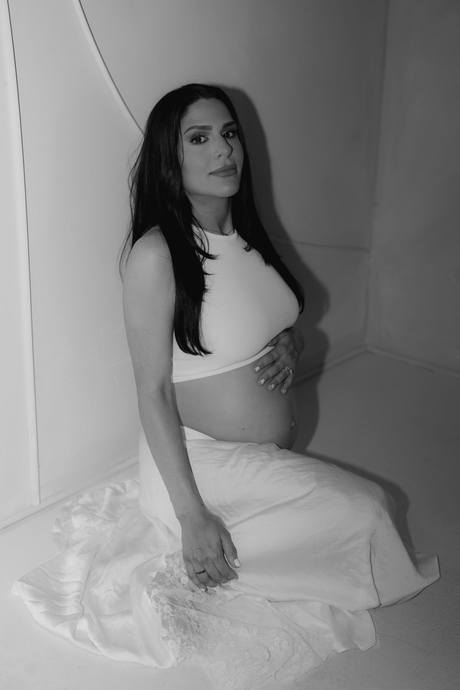 Black and white maternity portraits showing a woman in a white top against a plain wall.