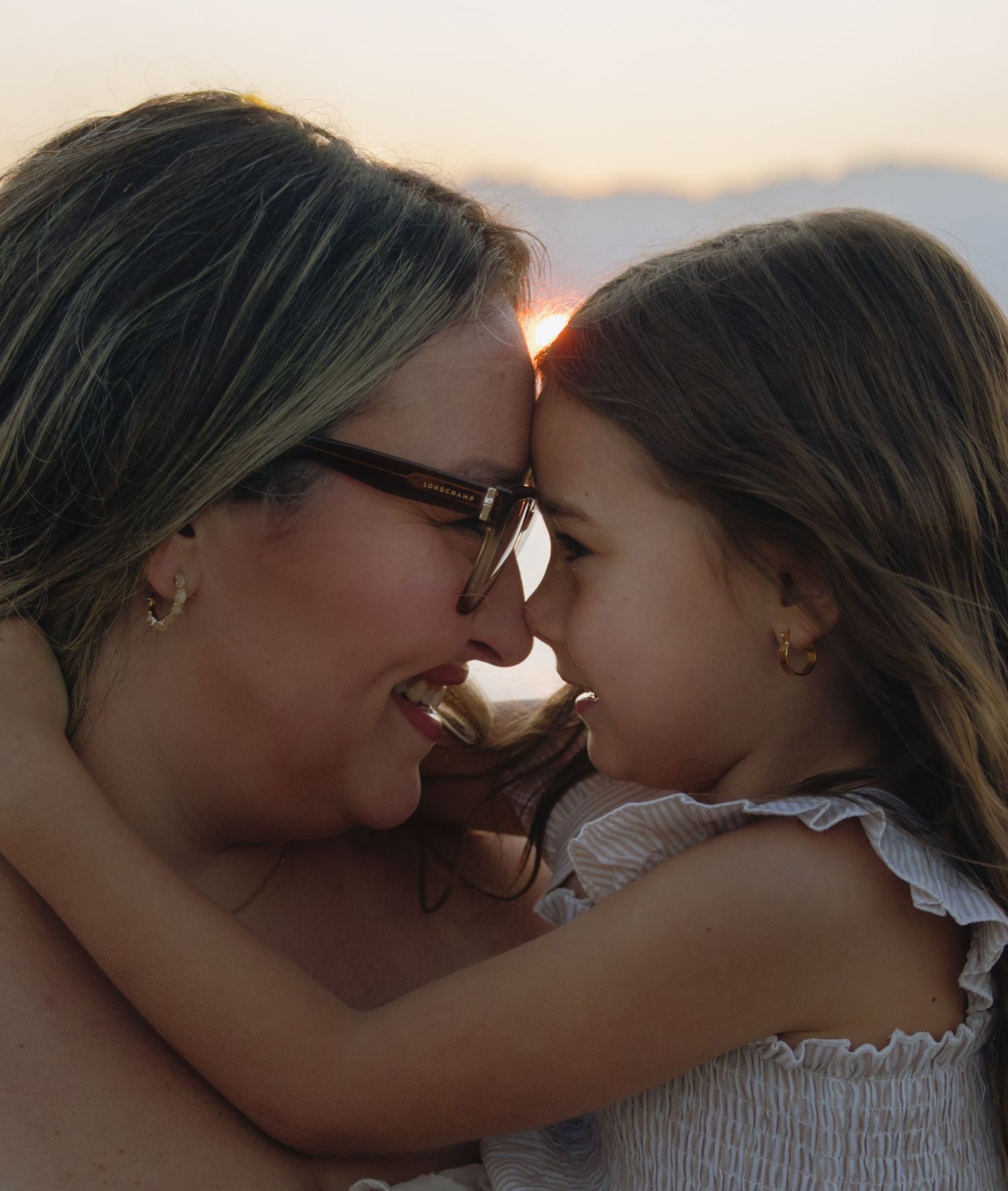 Two people share a close, joyful moment together against a sunset beach backdrop.