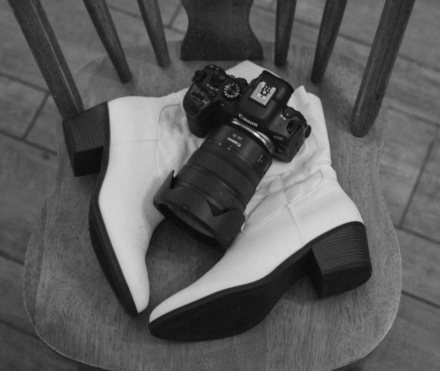 A black mirrorless camera sits on top of black and white platform boots resting on a wooden chair.