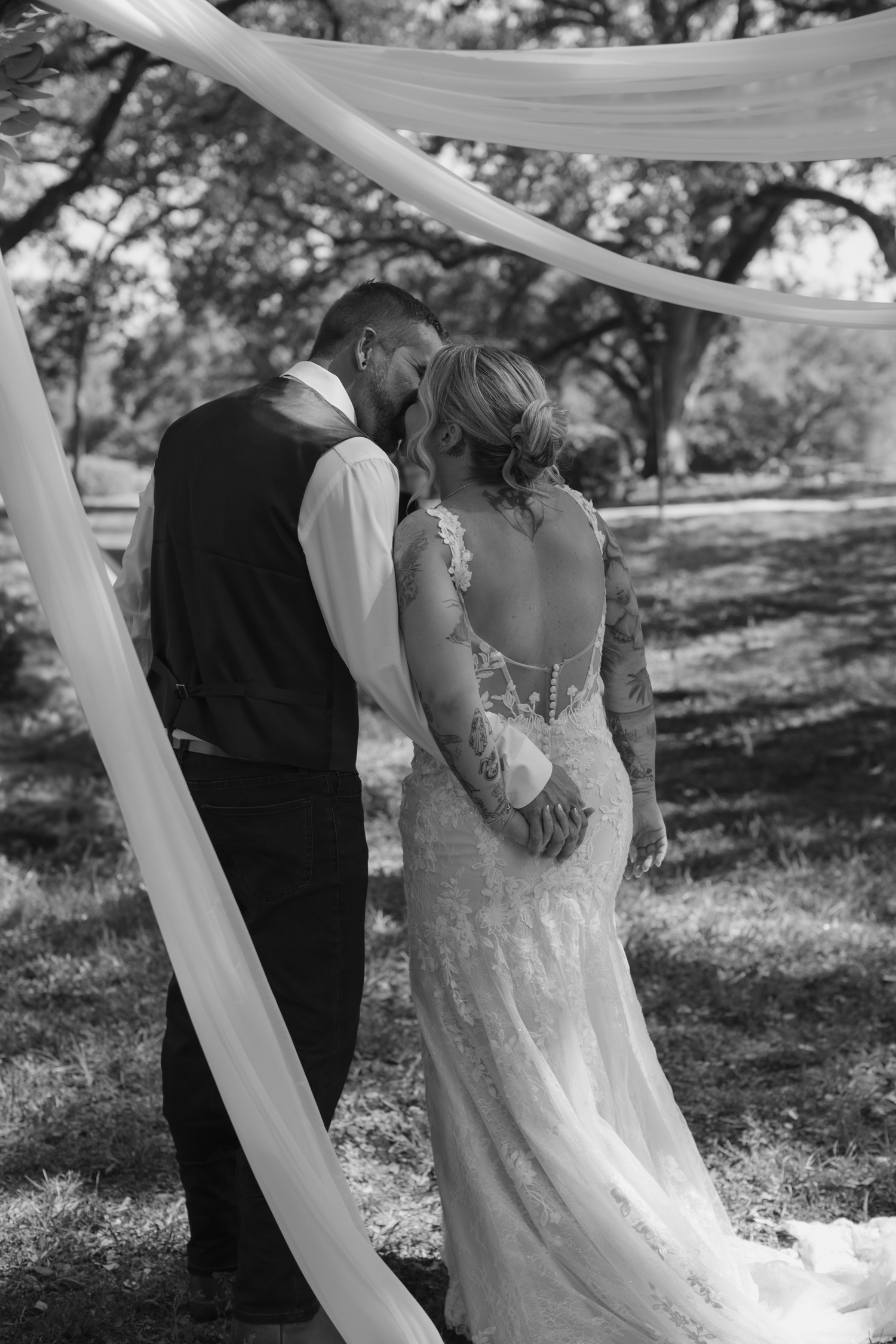 A romantic black and white wedding photo series showing a couple embracing under flowing white fabric in an outdoor setting.
