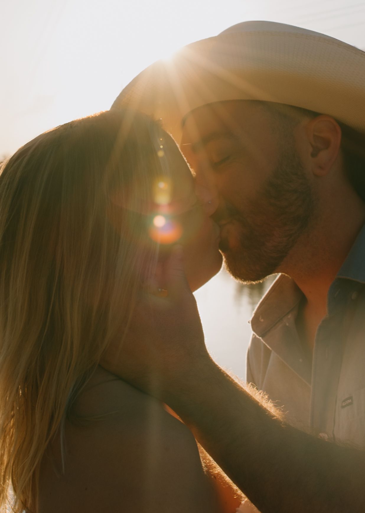 A romantic silhouette of a couple embracing in warm sunlight creating a dreamy, backlit glow effect.