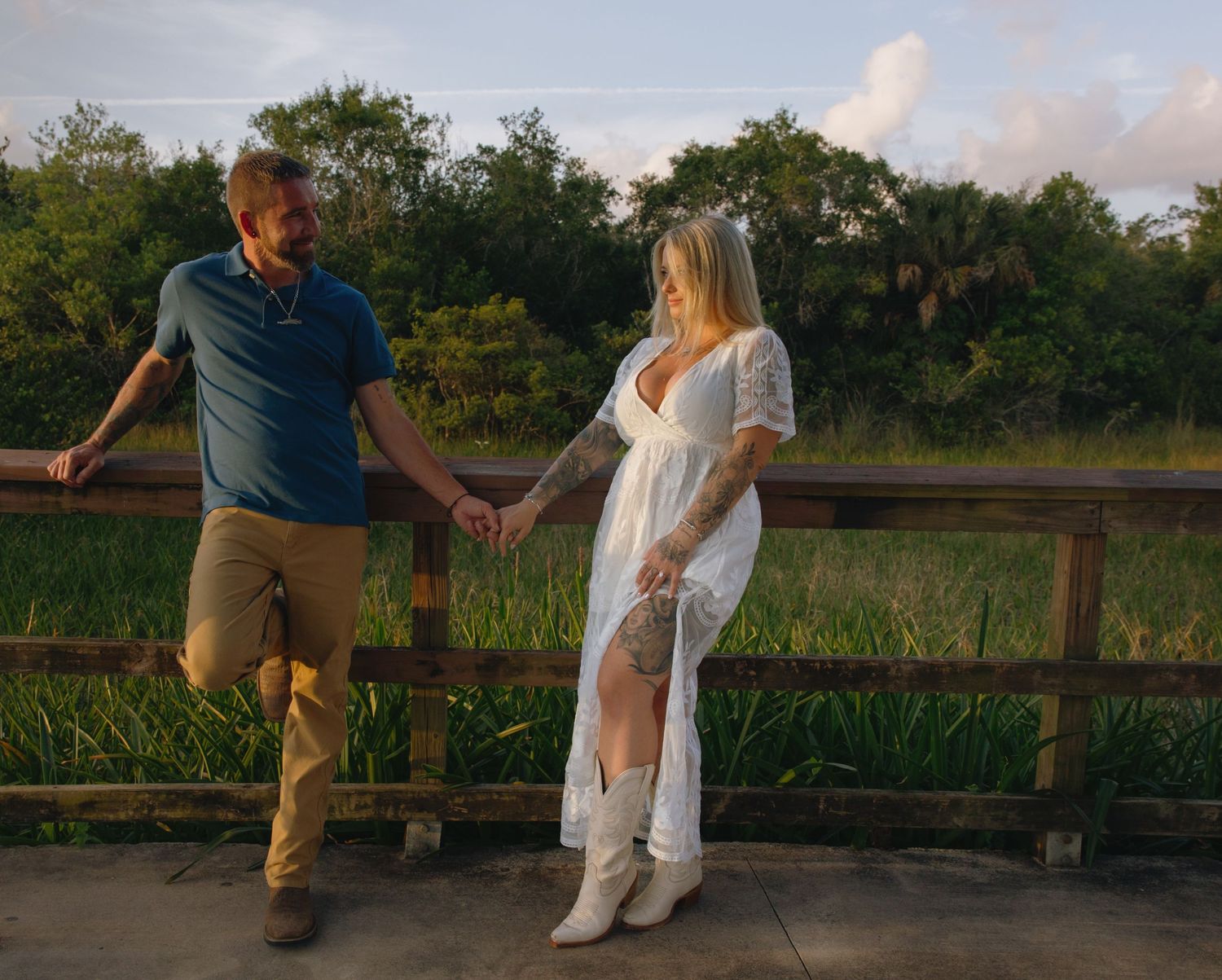 People sharing a romantic moment on a wooden boardwalk in a natural setting during sunset.