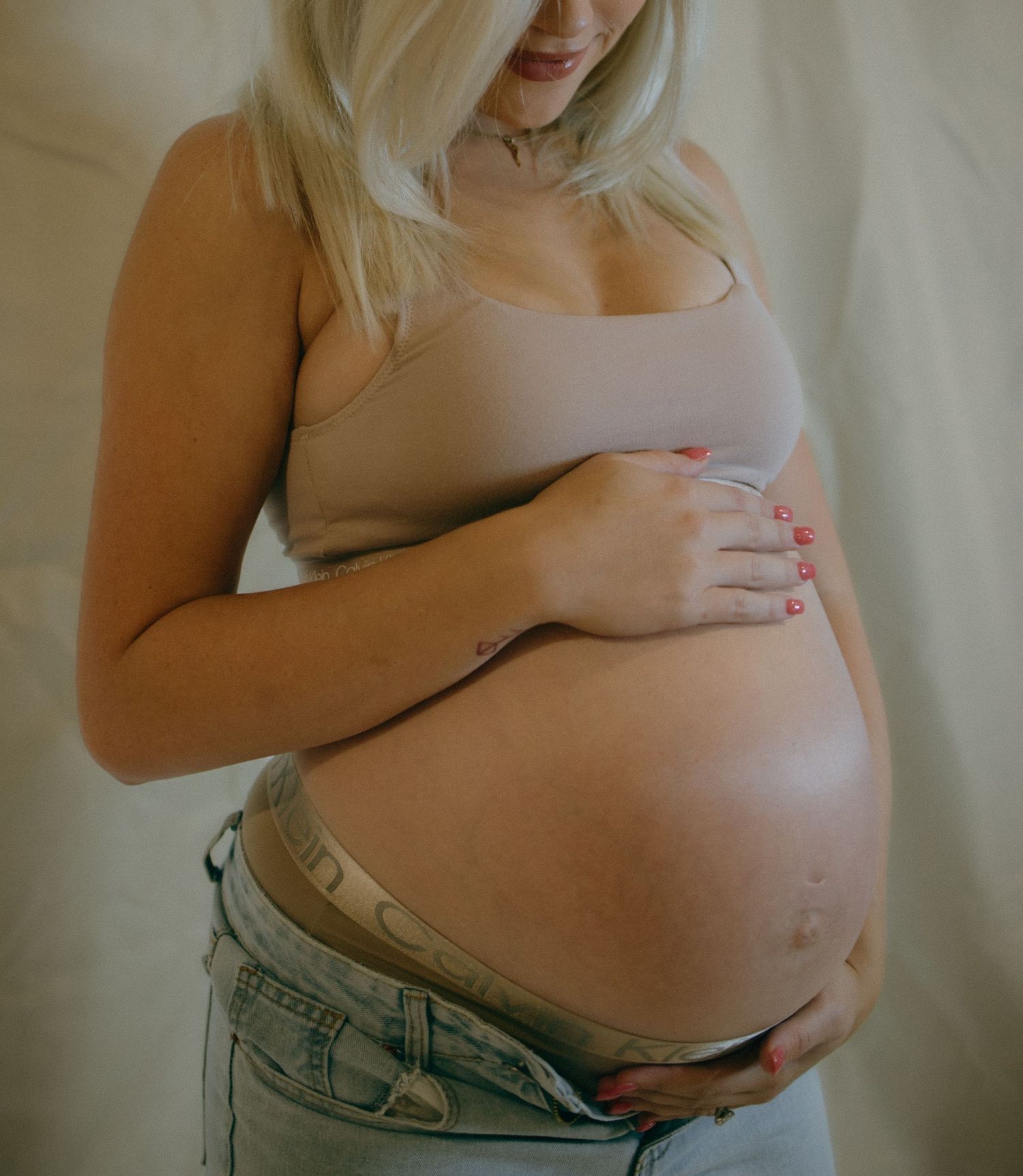 Expectant mother in beige top and jeans cradling baby bump.