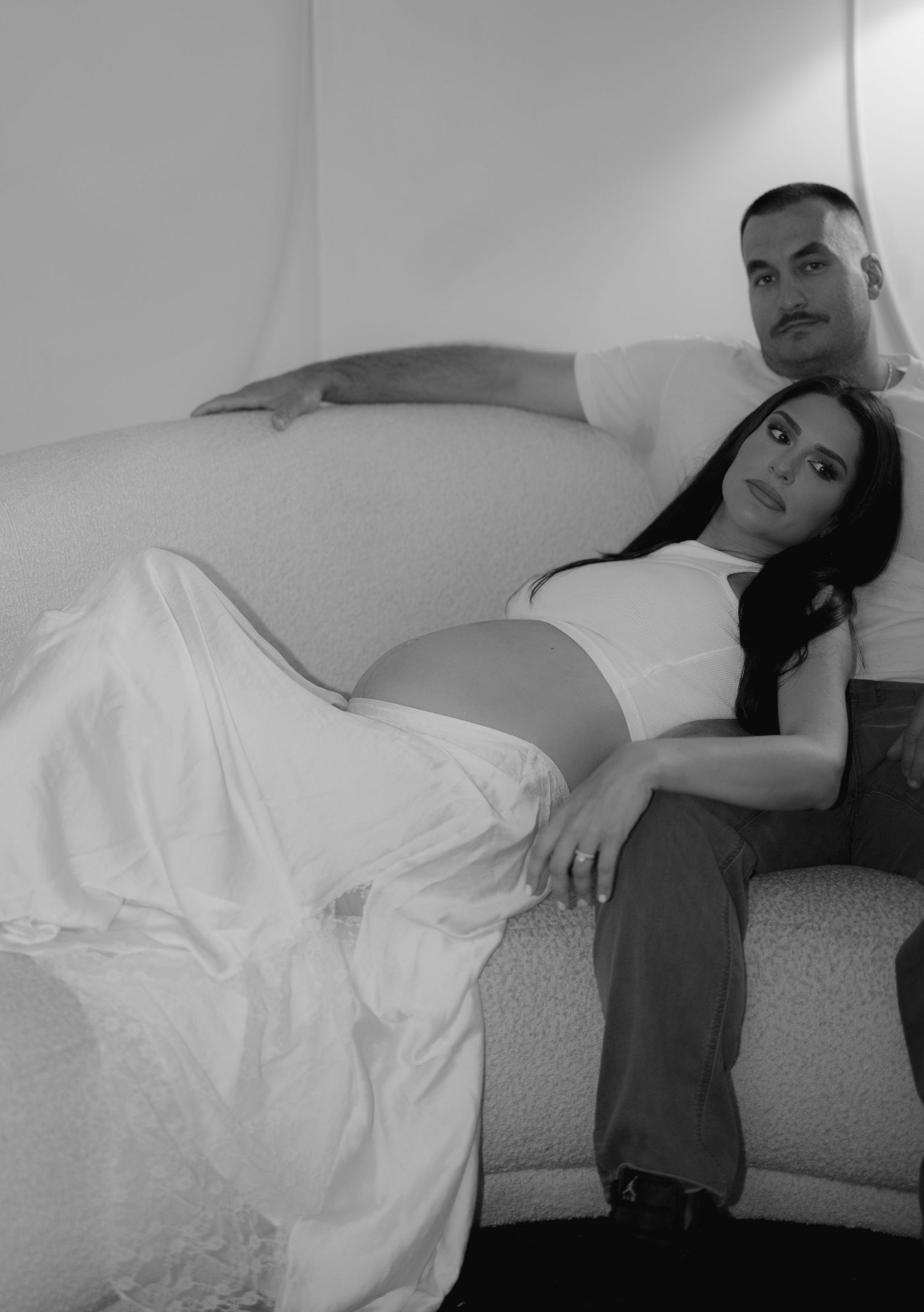 Maternity photography sequence showing someone in a white dress reclining on a sofa.