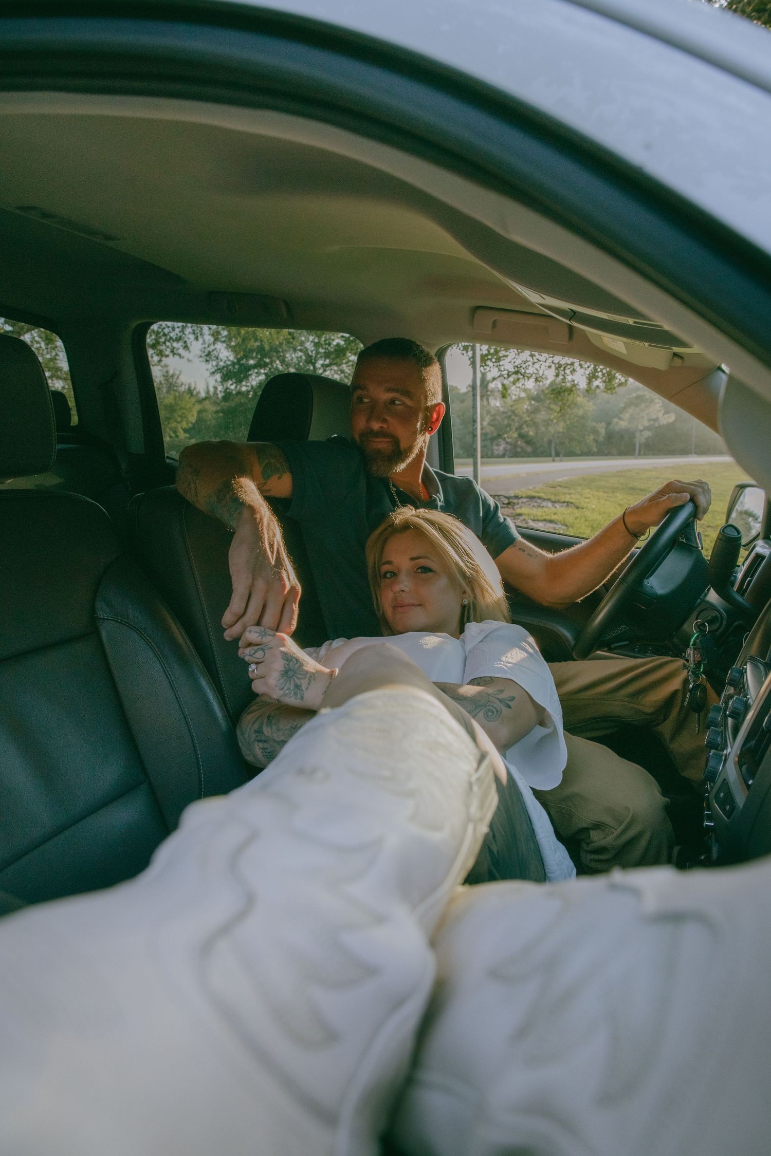 A couple relaxes together in a car with sunlight filtering through the window during a casual photoshoot.