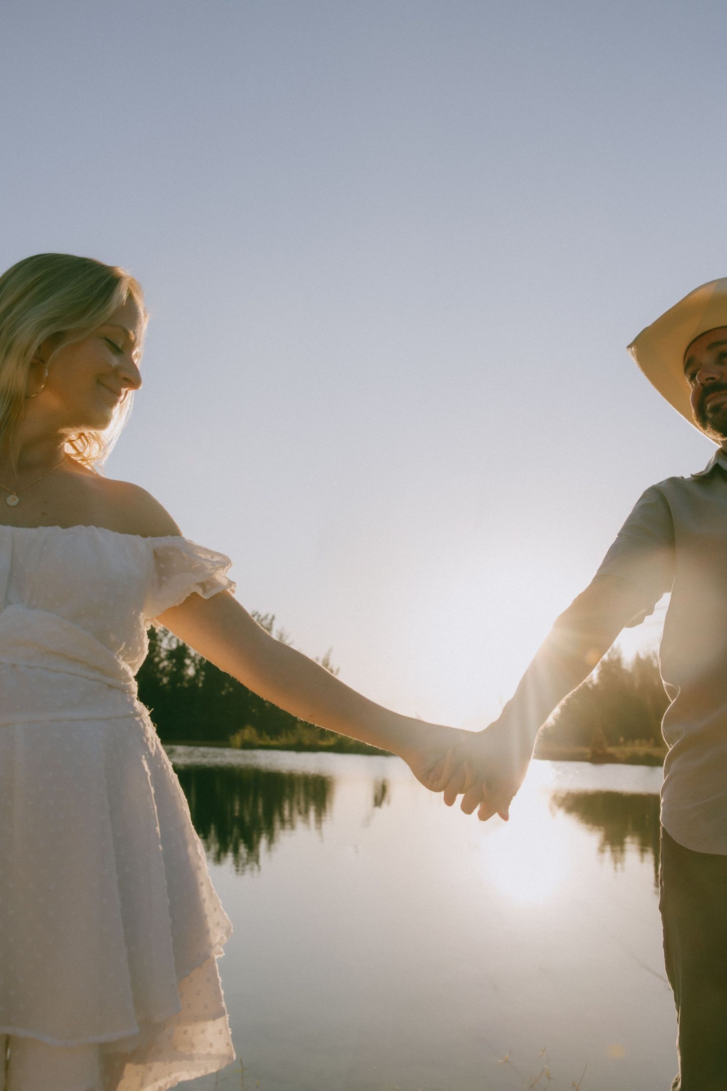 Silhouetted couple holding hands and walking together against bright sunlight during a romantic sunset moment.