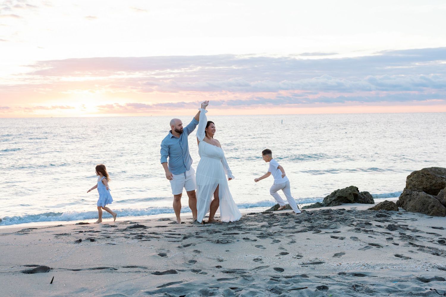 Family enjoying a sunset beach walk along the shoreline with waves crashing in the background.