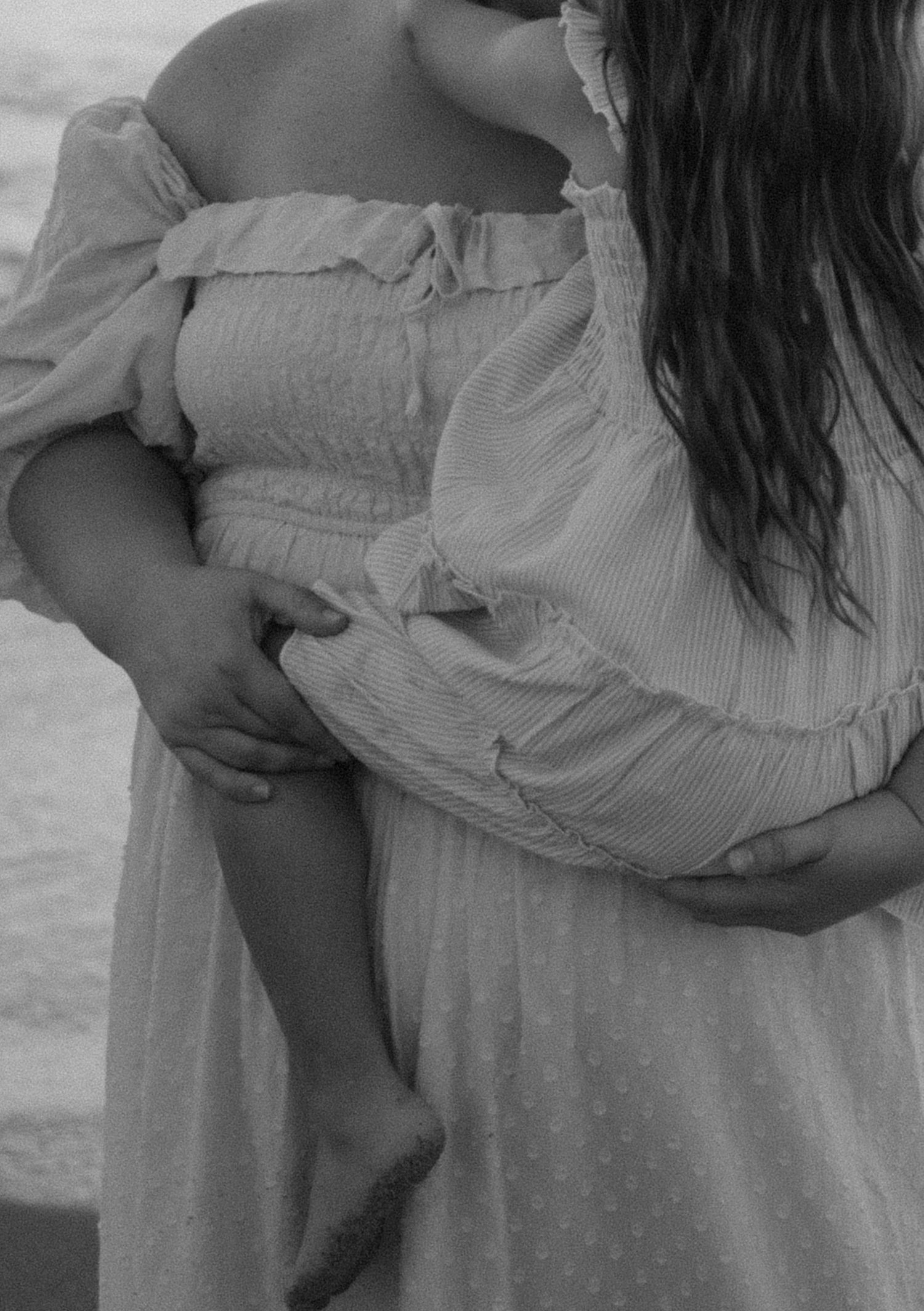 A series of black and white photos showing someone holding a baby in a white dress against a light background.