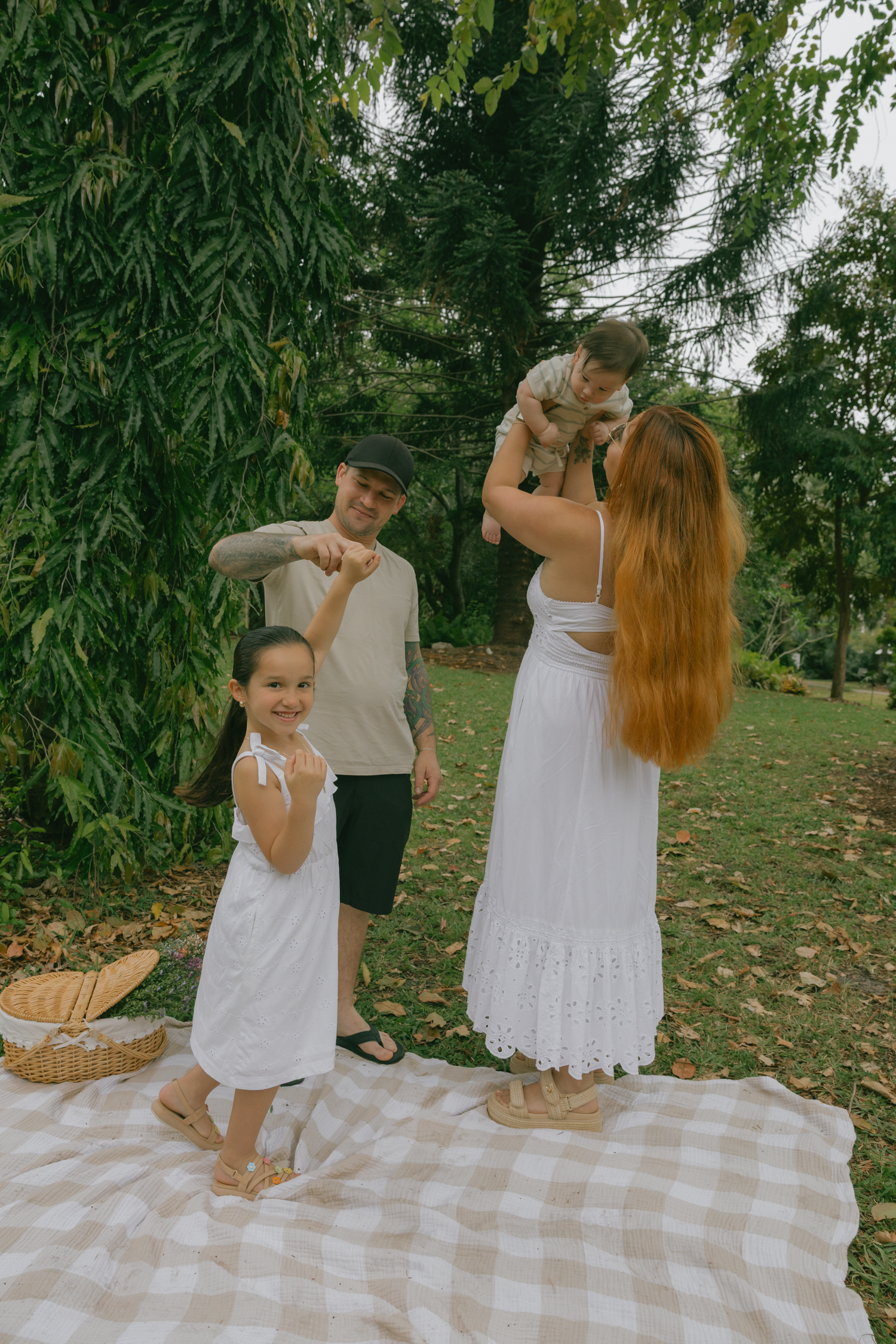 Family picnic scene on checkered blanket surrounded by lush greenery.