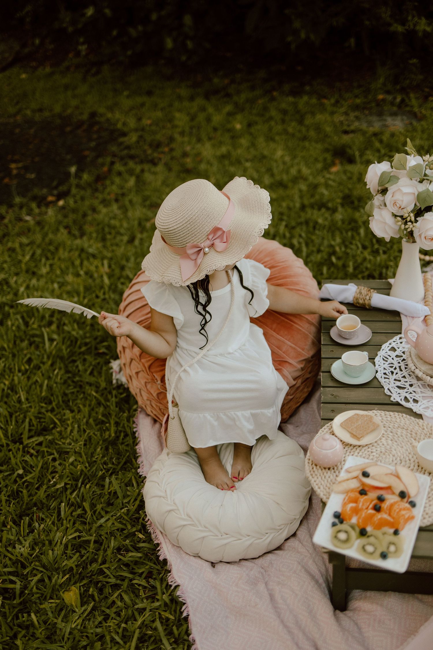 Garden tea party with vintage decor and white floral arrangements on picnic blanket.