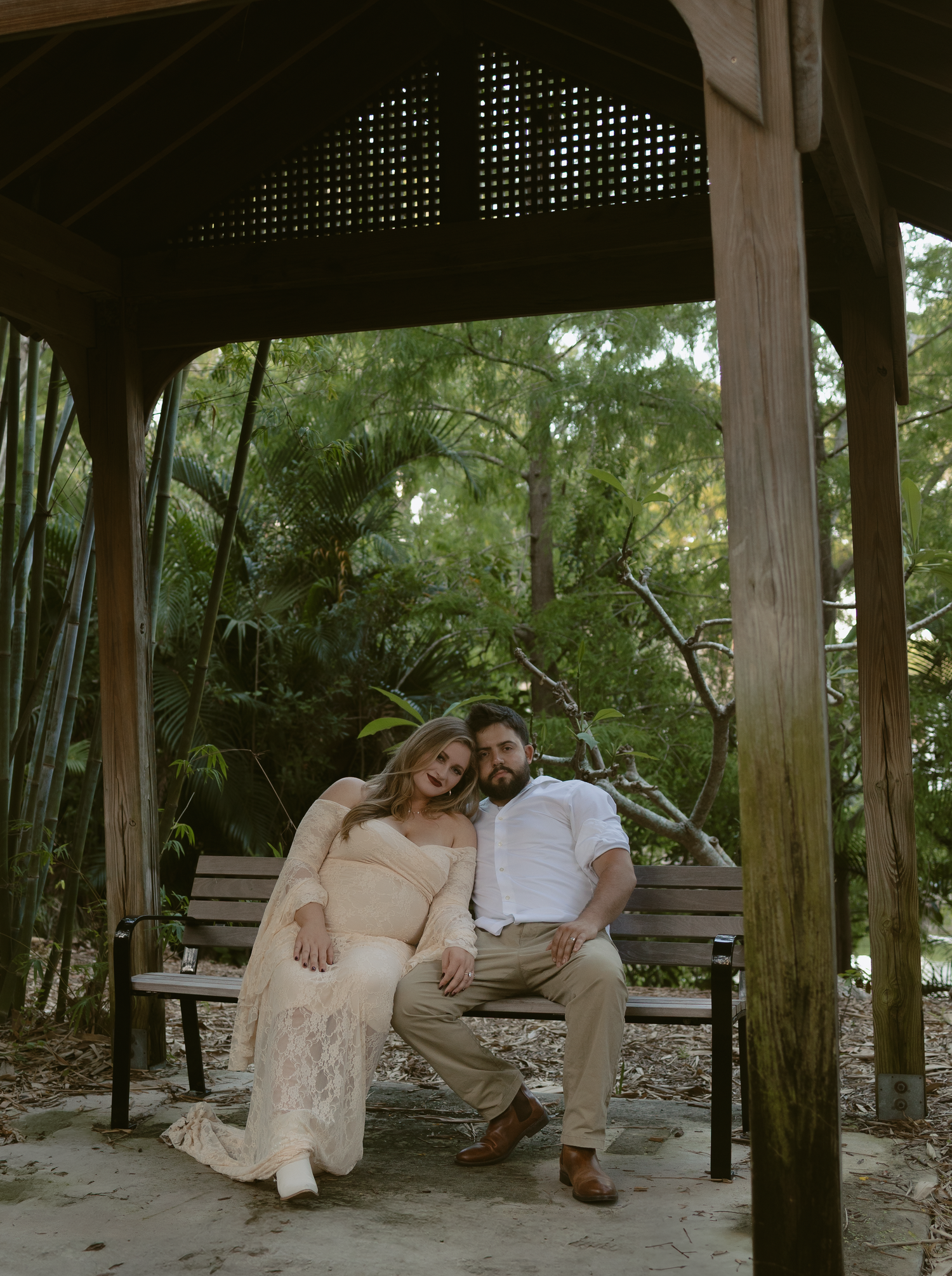 Romantic couple sitting together on wooden swing in lush garden gazebo during sunset photoshoot.