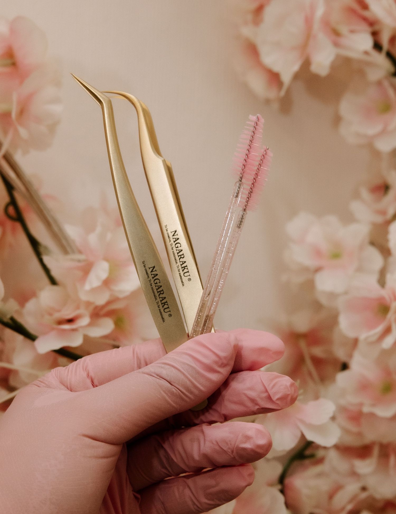 Close-up view of pink tweezers and tools arranged with delicate cherry blossoms in the background.