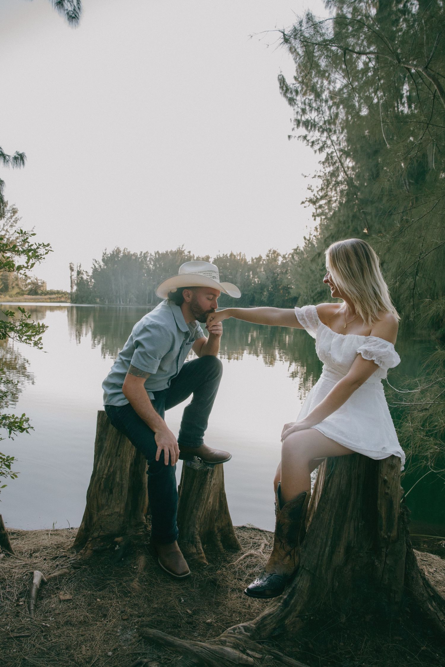 Lakeside photo session with western-styled outfits on tree stumps.