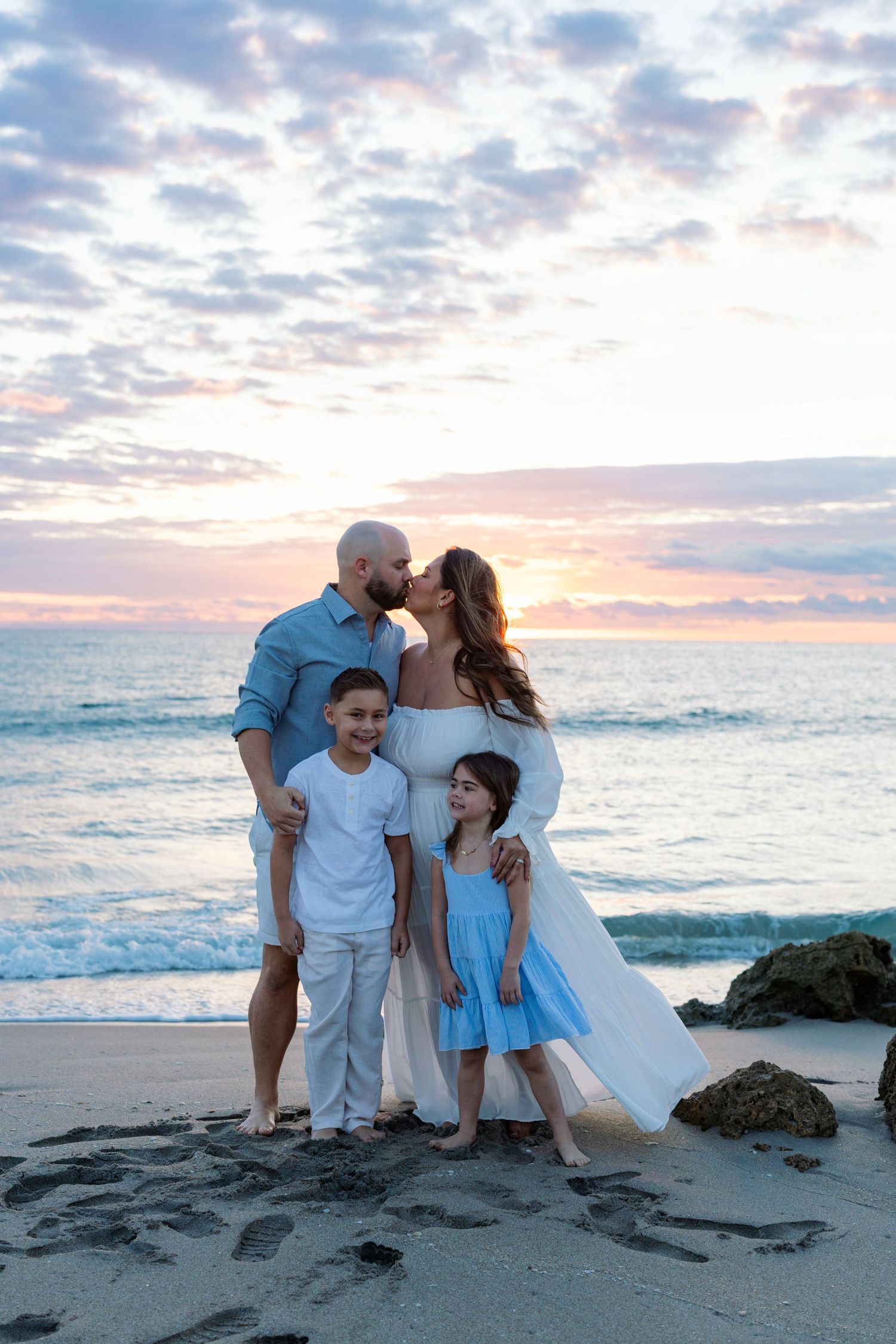 Family enjoying a sunset photo session at the beach with ocean waves and cloudy sky in the background.