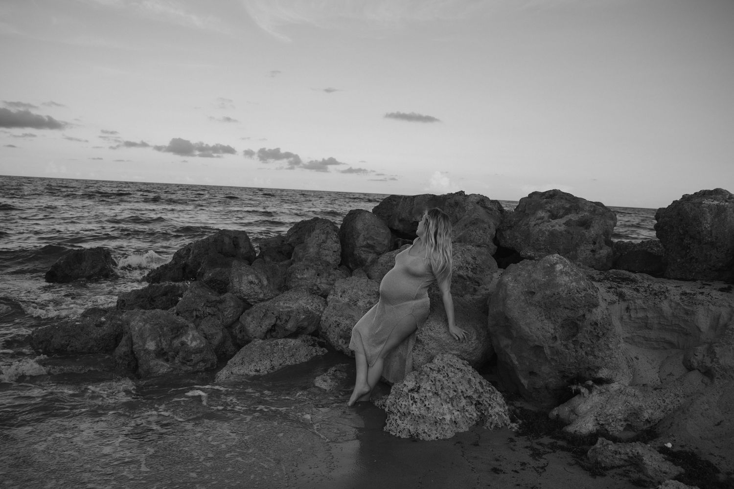 Black and white maternity photo featuring silhouette against rocky beach landscape.