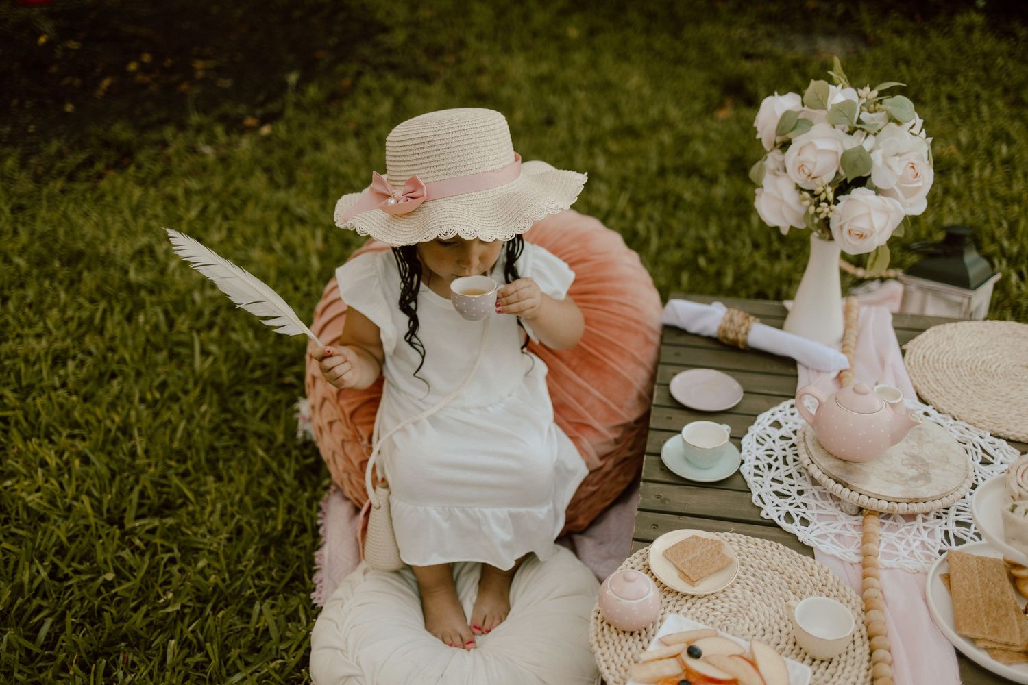 Outdoor tea party scene with soft pink cushions and elegant table settings.