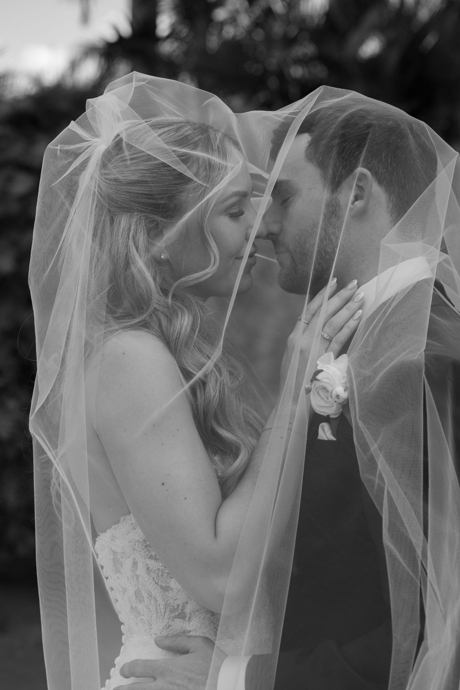 A romantic black and white wedding photo showing a couple sharing an intimate kiss beneath a flowing veil.
