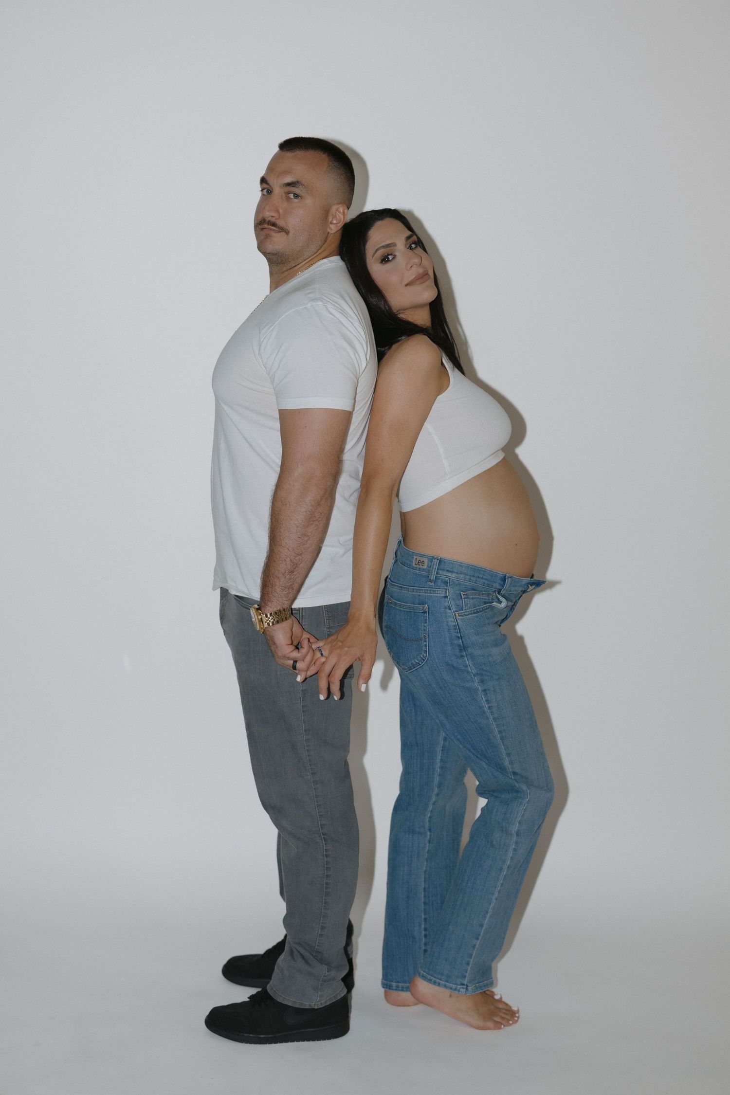 Two people in casual clothing sit back to back against white backdrop in series of minimalist artistic poses.