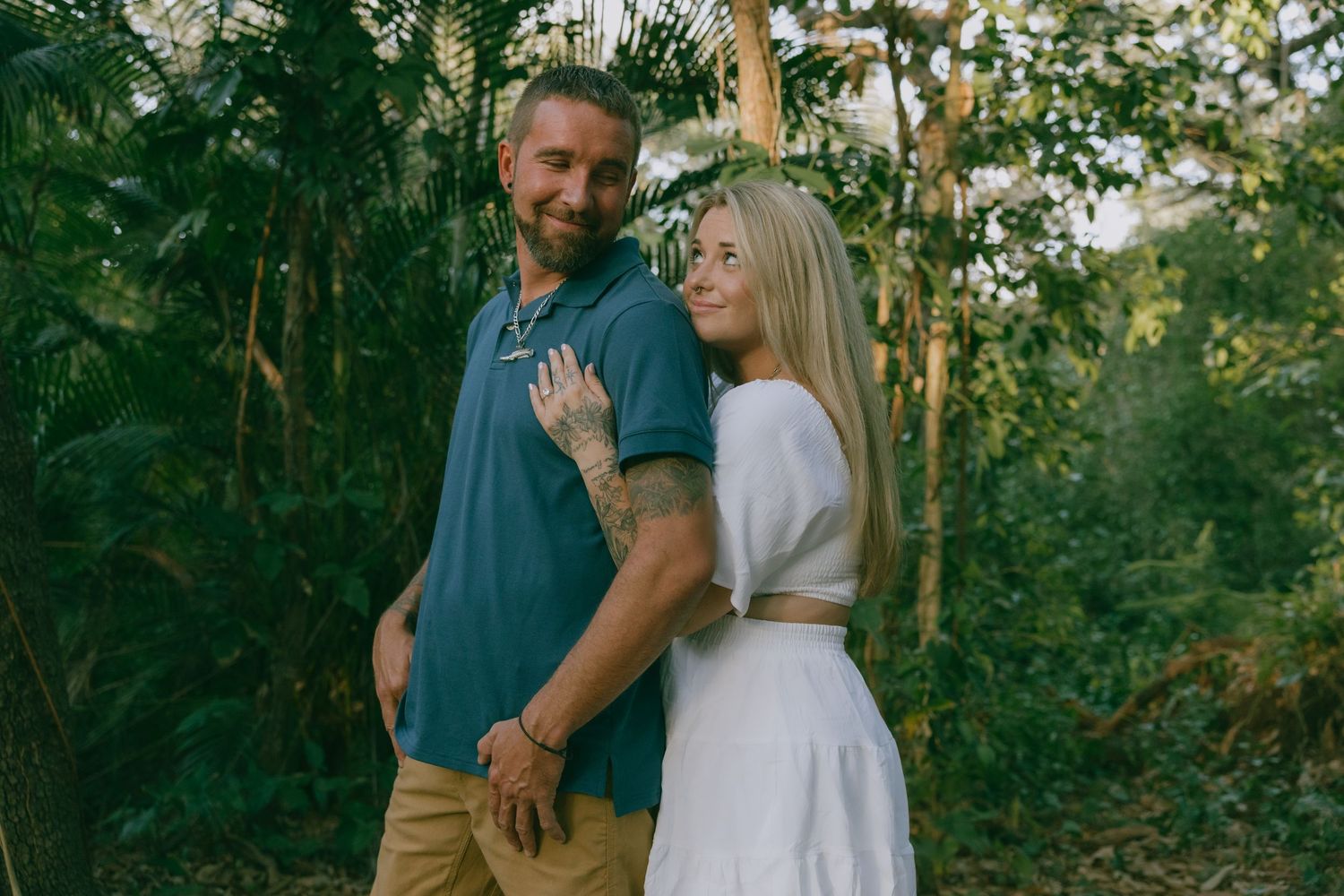 Couple posing together outdoors in a lush green natural setting.