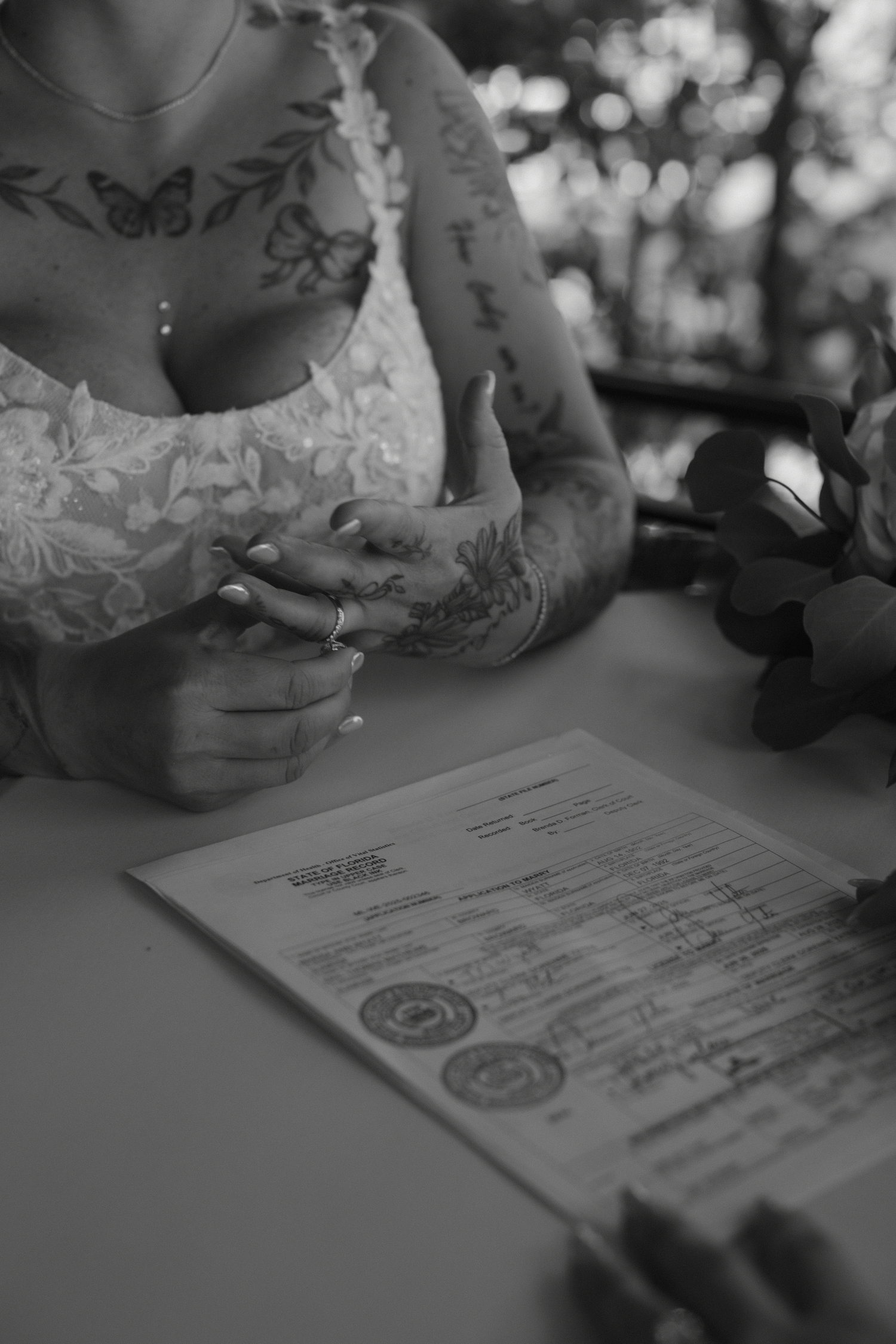 Black and white close-up of hands signing a marriage certificate during a wedding ceremony.
