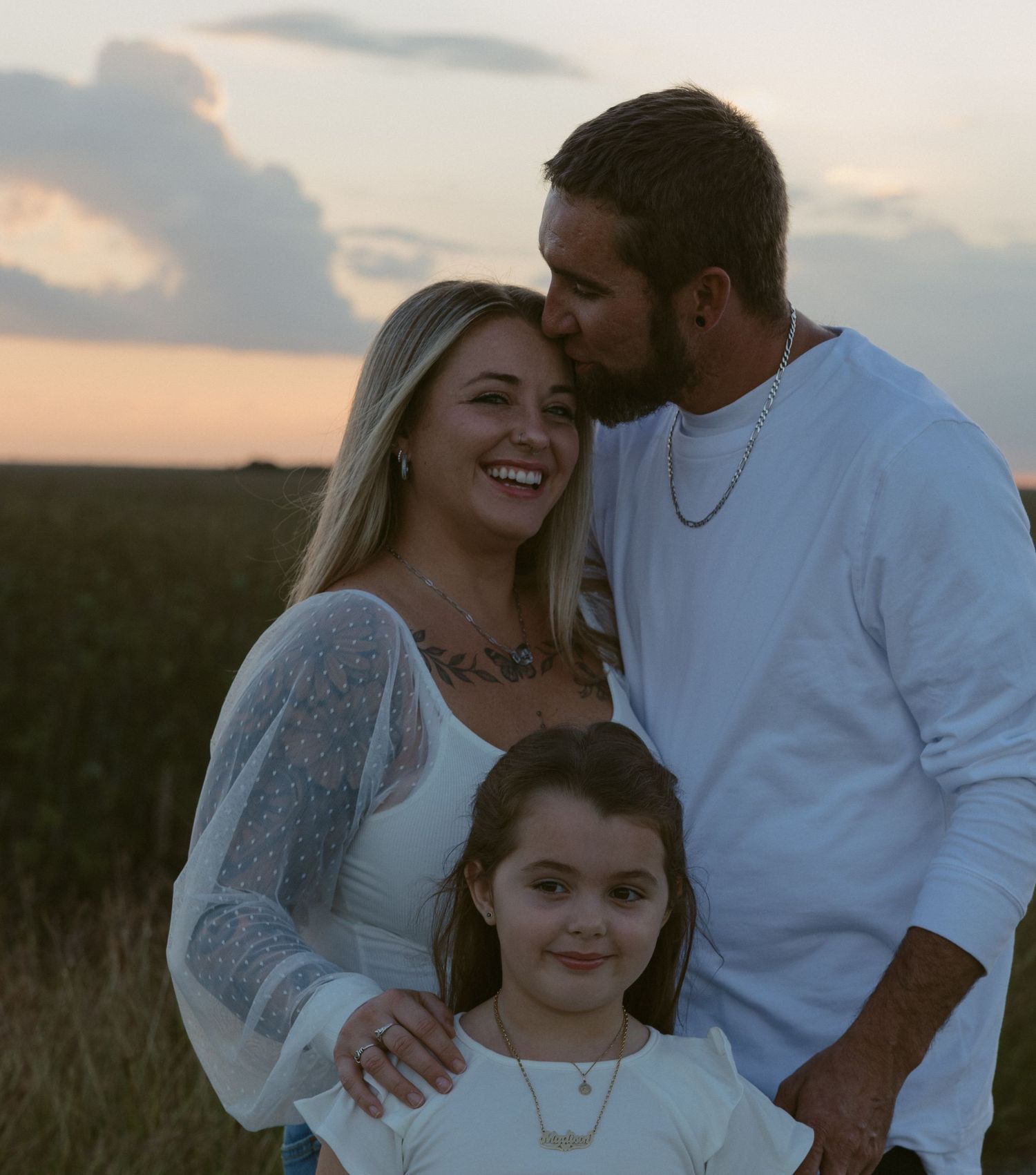 Family sharing tender moments together in a grassy field at sunset.
