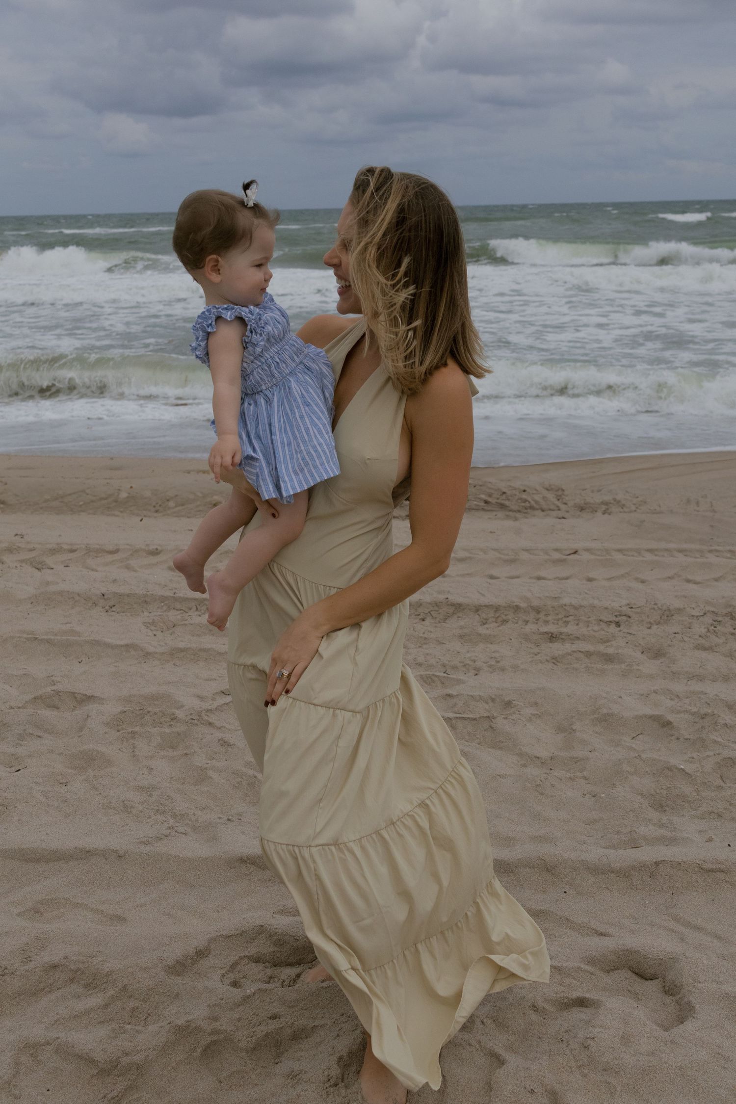 A tender beach moment captured as two people share an embrace by the ocean waves on a cloudy day.