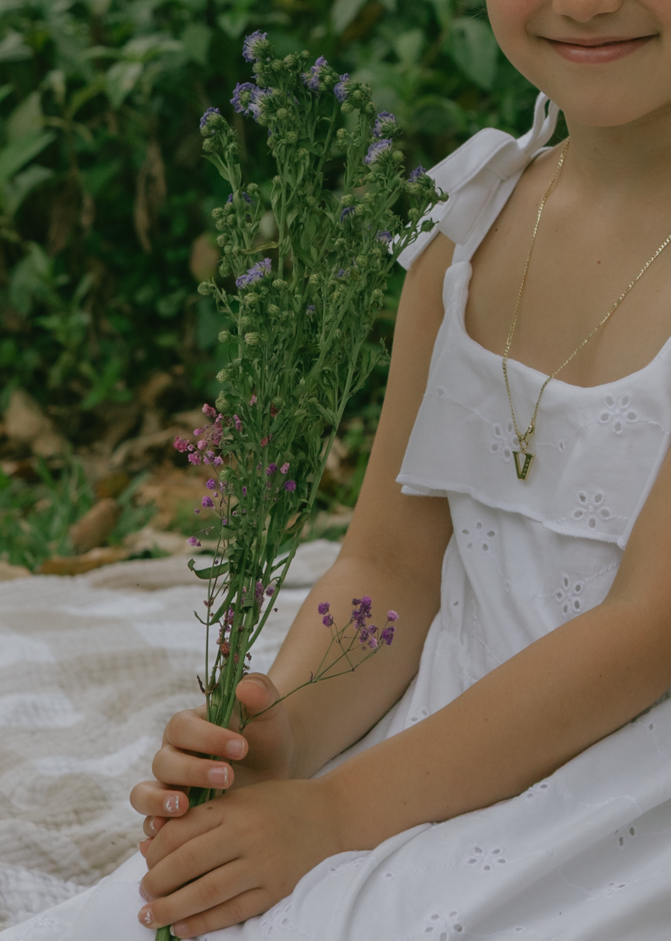 A delicate purple wildflower is held gently against a white dress in a natural outdoor setting.