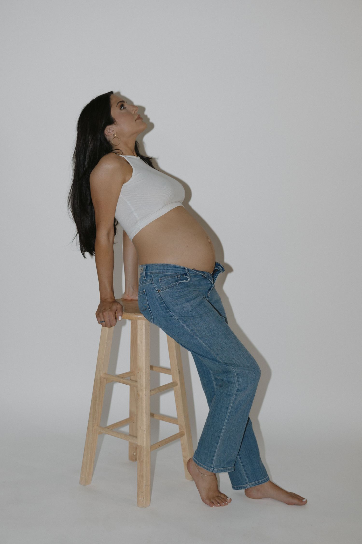 Minimalist maternity portraits showing different poses on wooden stool against white wall.