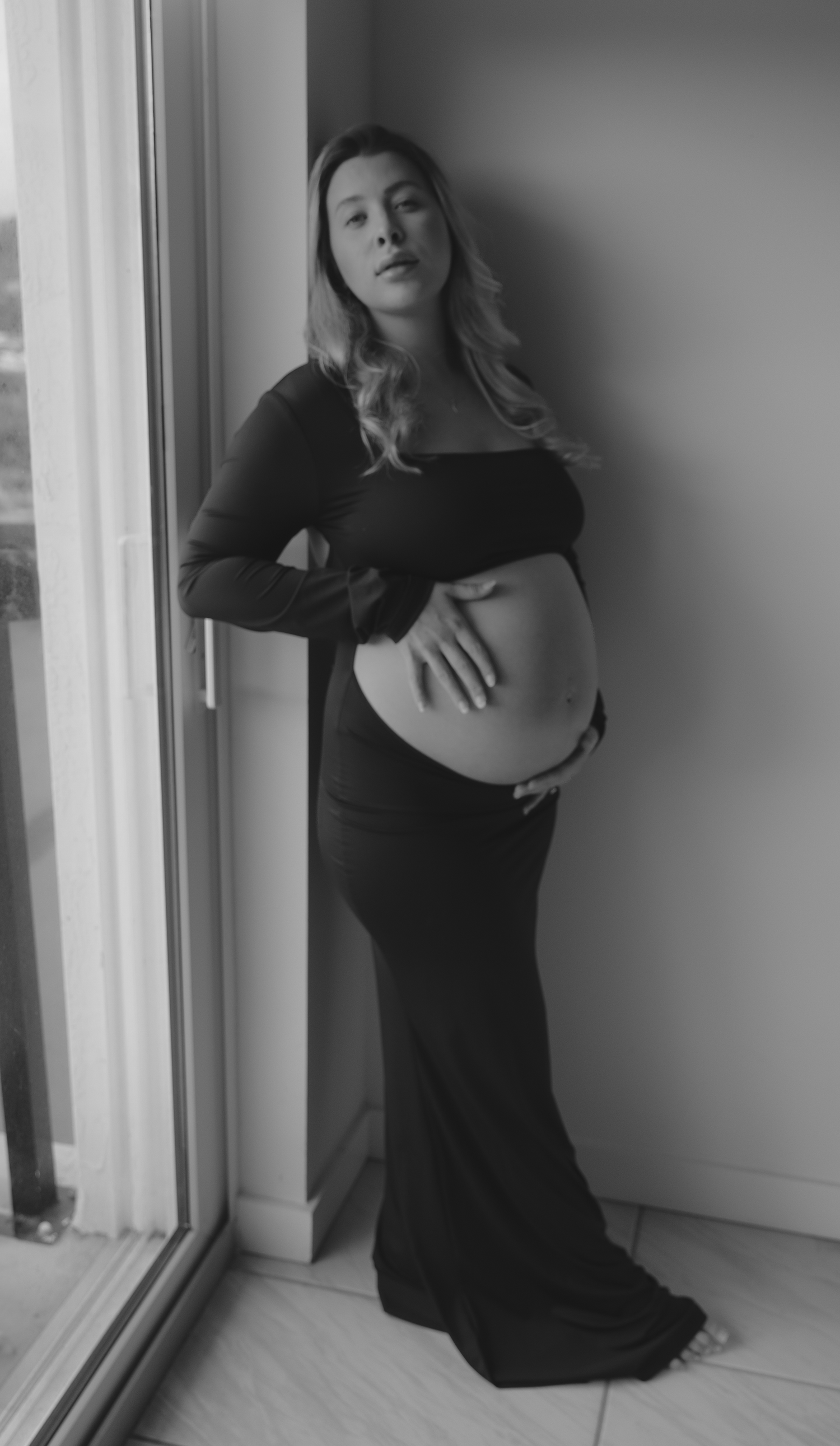 Dramatic black and white portrait against windowsill in natural light.