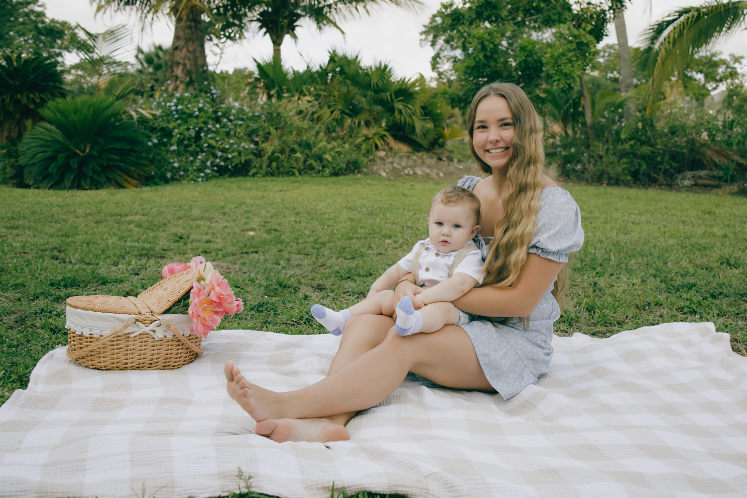 Tender outdoor family moment captured on a white blanket in a lush tropical garden setting.
