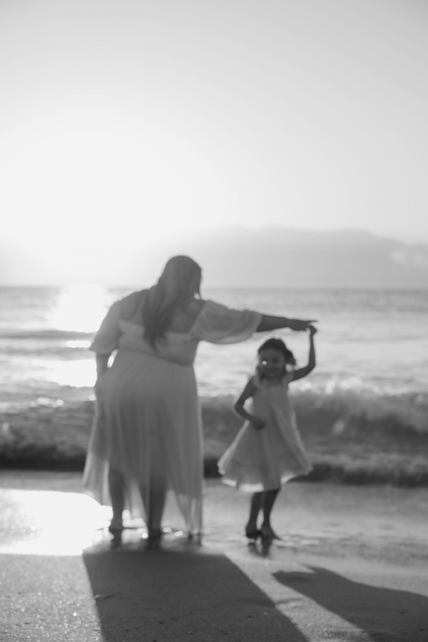 Black and white silhouettes of figures dancing and playing on beach with waves in background.