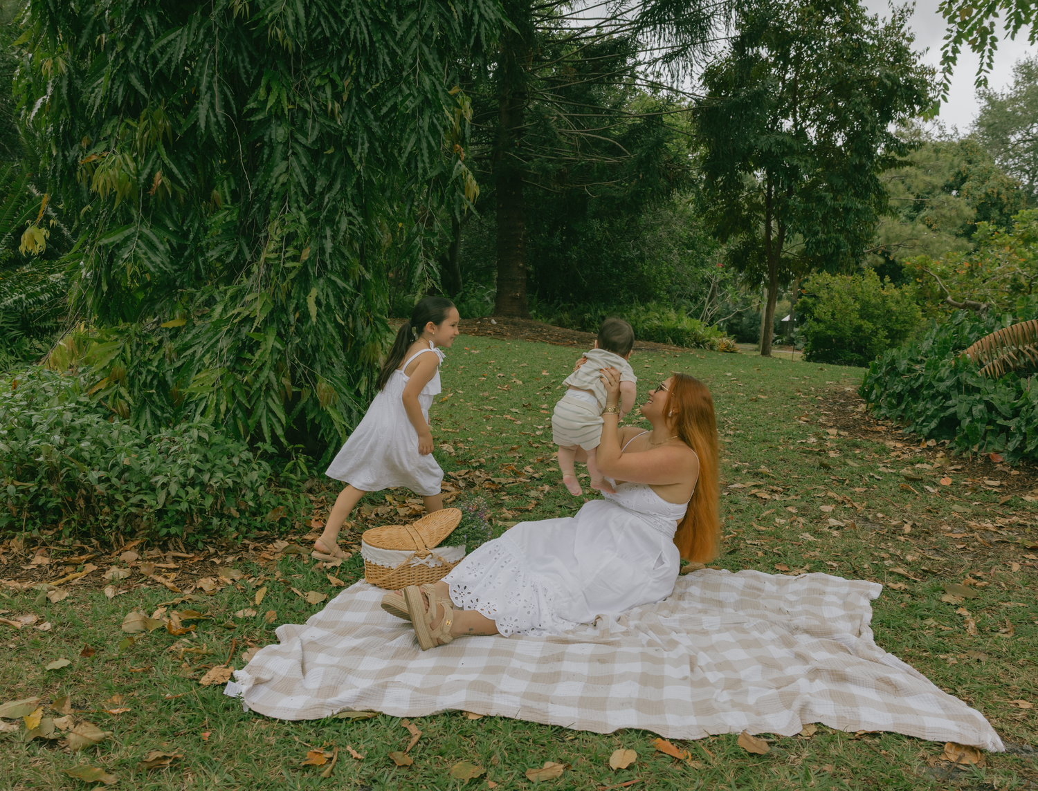 Family having fun and playing on checkered picnic blanket in a park setting.