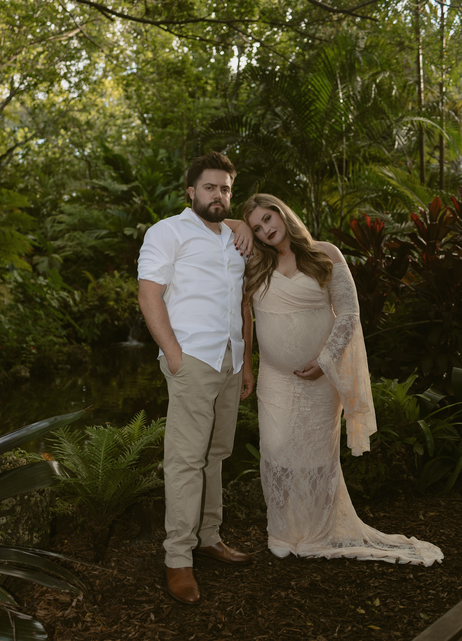 A couple in white and beige attire shares an intimate moment together in a lush garden setting.