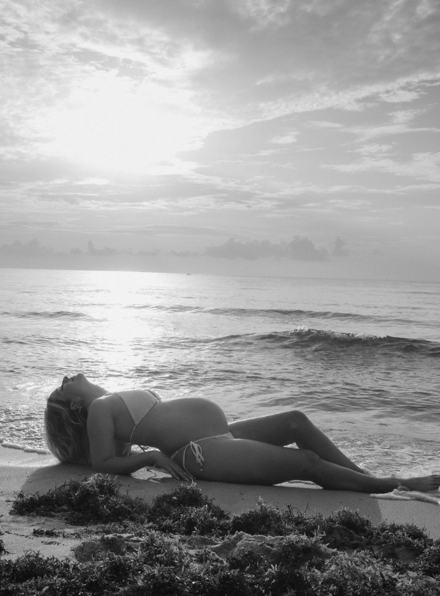 A silhouetted figure rests on a beach during sunrise with waves rolling in the background.