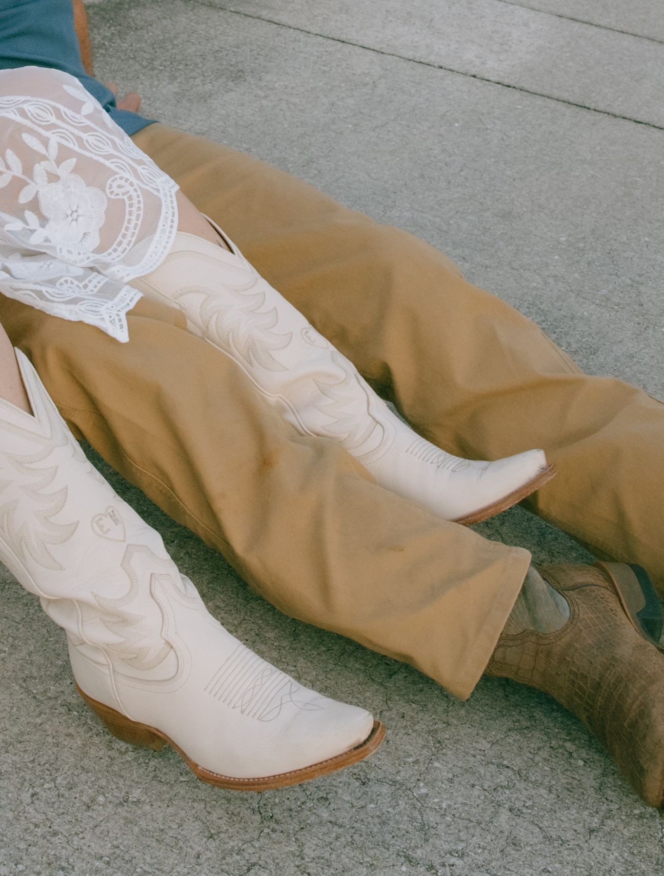 White embroidered cowboy boots paired with tan pants on concrete ground.