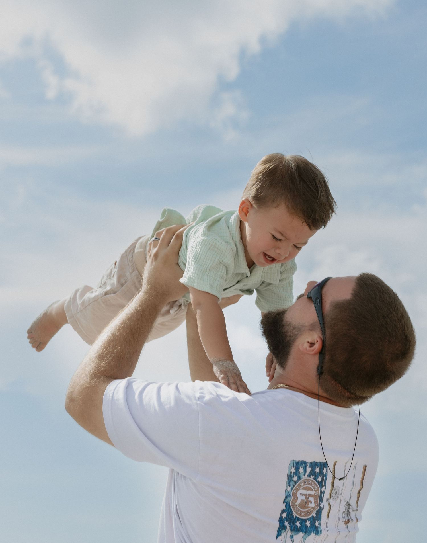A parent lifts a small child in the air against a bright blue sky background in a series of joyful moments.